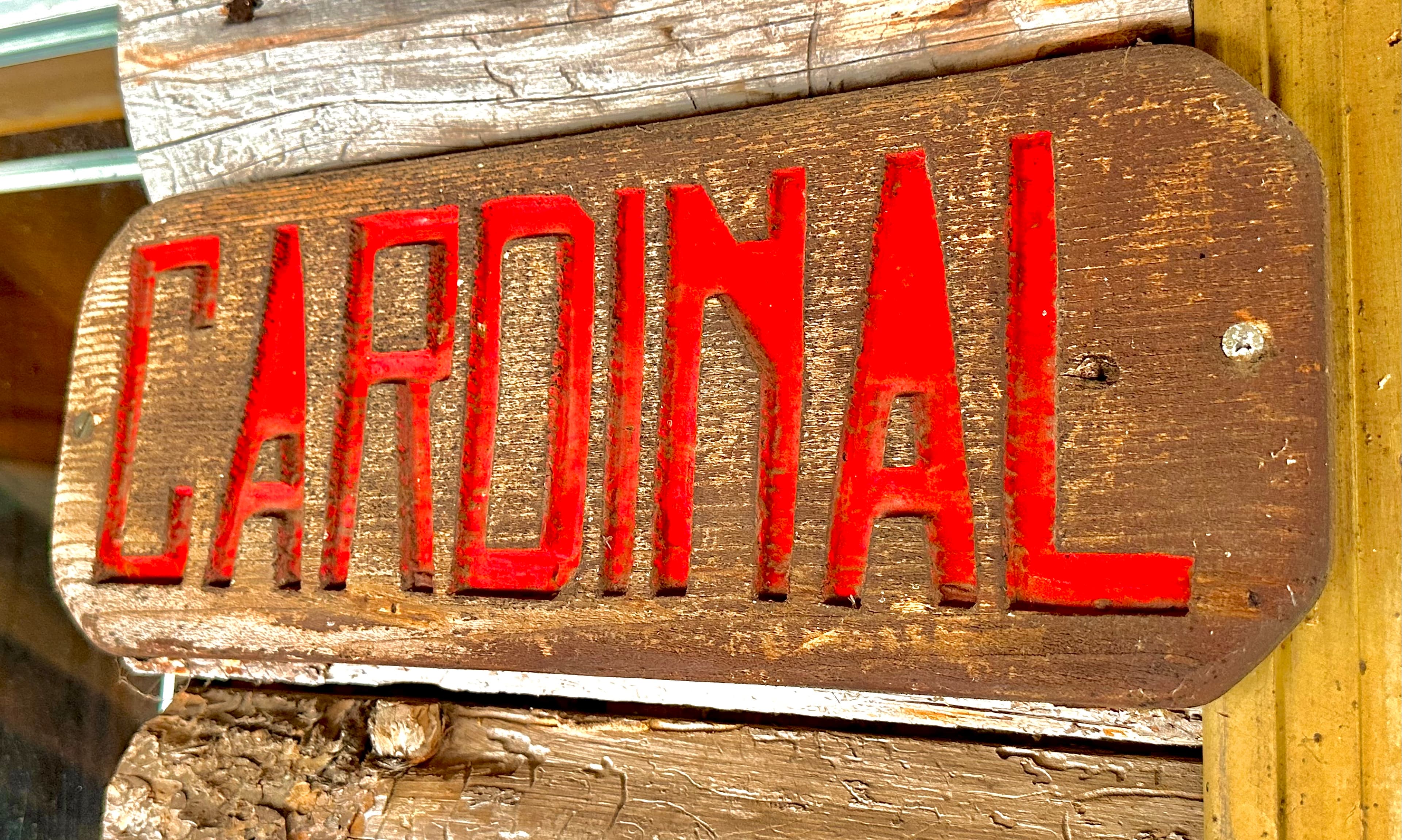 A wooden sign with "CARDINAL" painted in bold red letters.