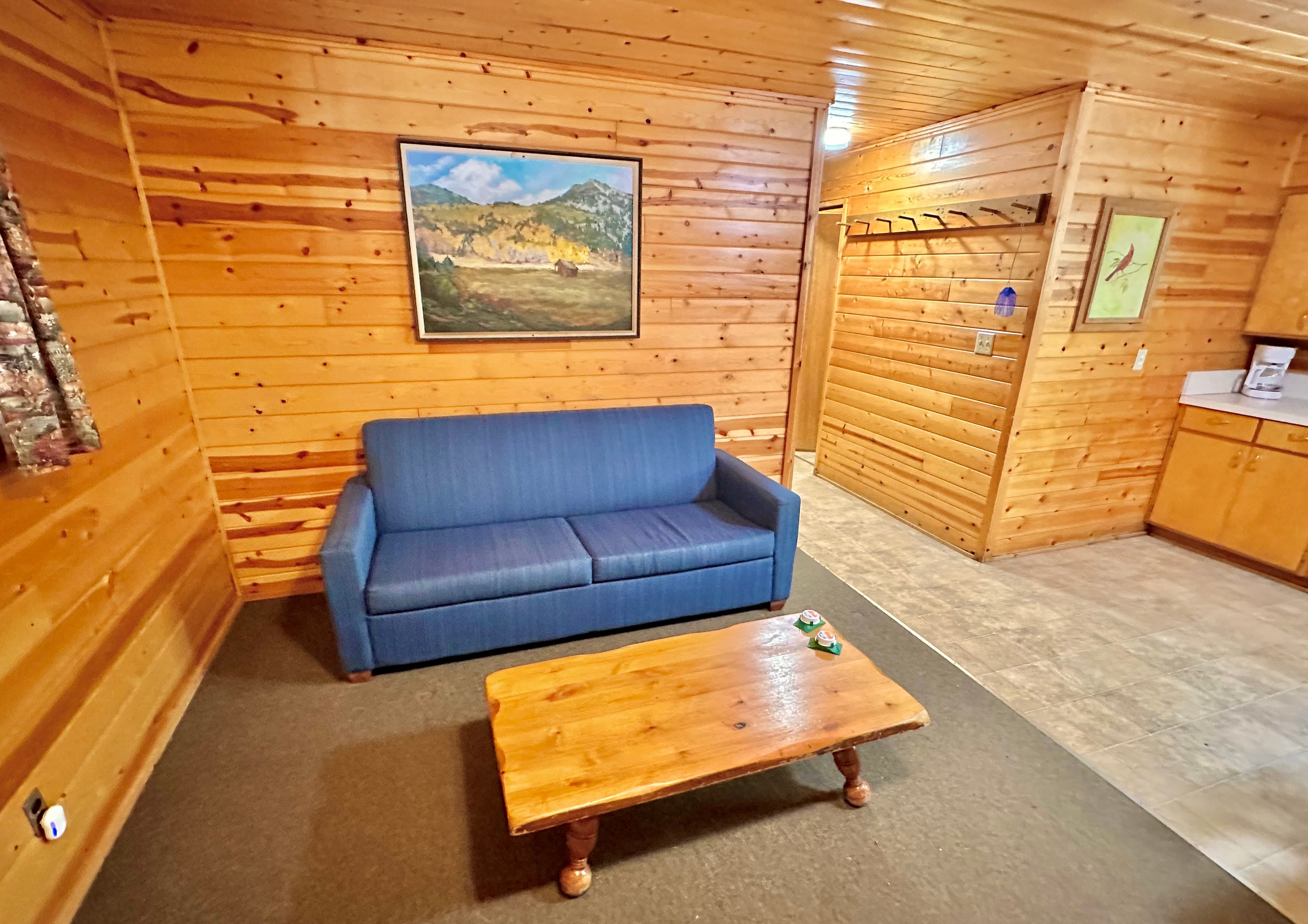 A cozy wooden cabin interior featuring a blue sofa, a wooden coffee table, and a painting on the wall.