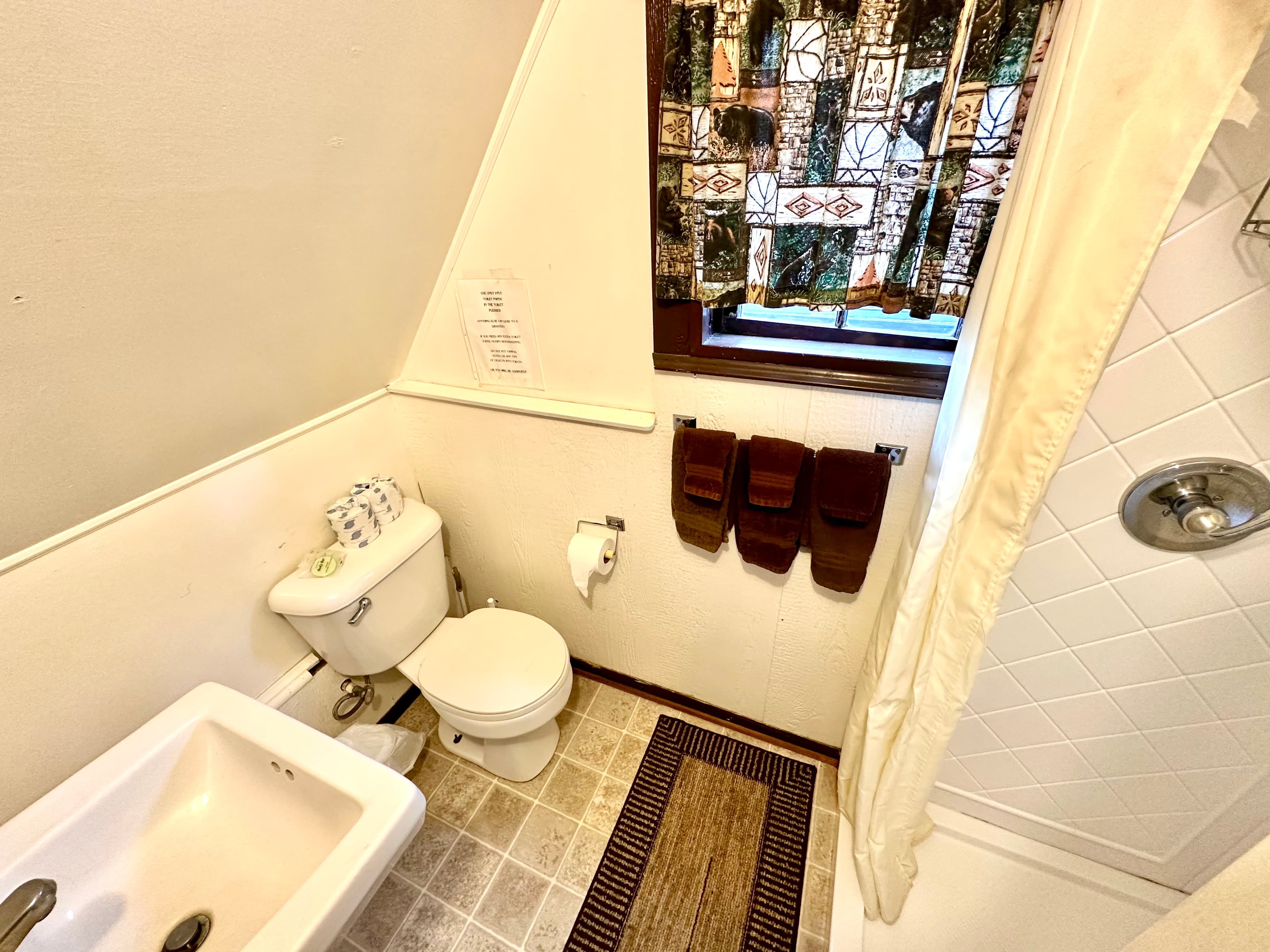 A small bathroom featuring a toilet, sink, shower, and brown towels hanging on the wall.