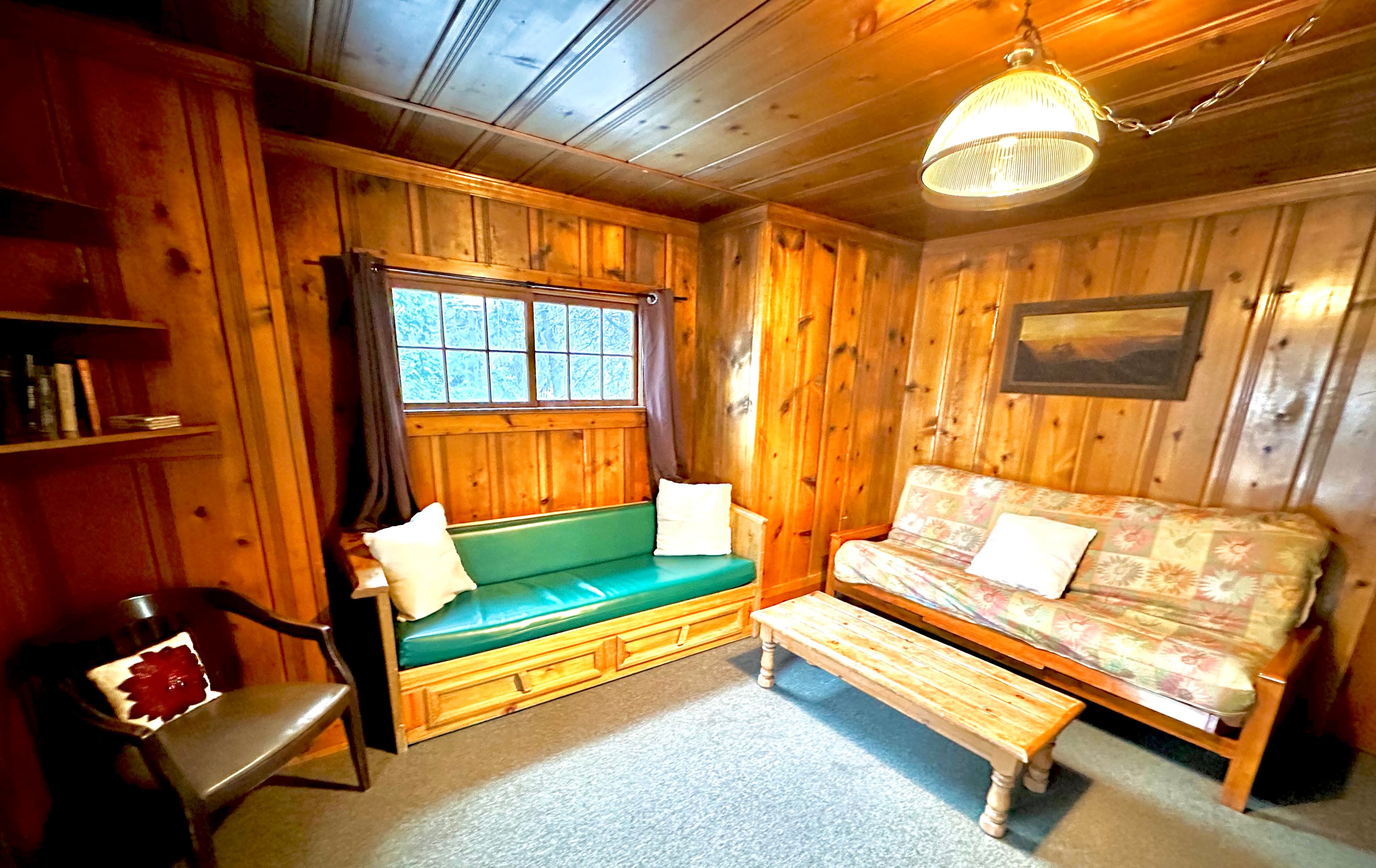 A cozy, wooden-paneled sitting area with a green bench, floral sofa, and a coffee table.