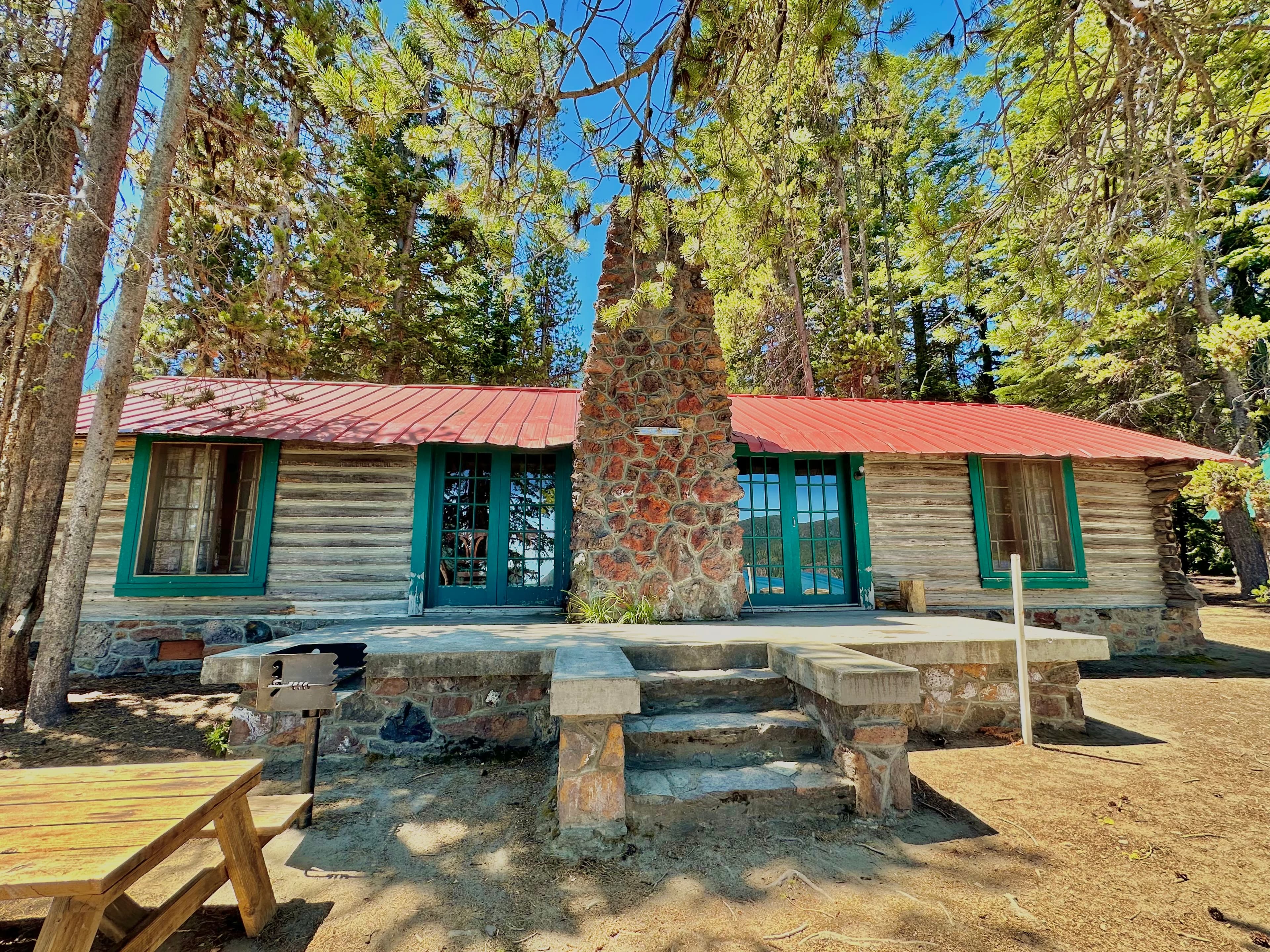 A rustic wooden cabin with a stone chimney surrounded by tall trees.
