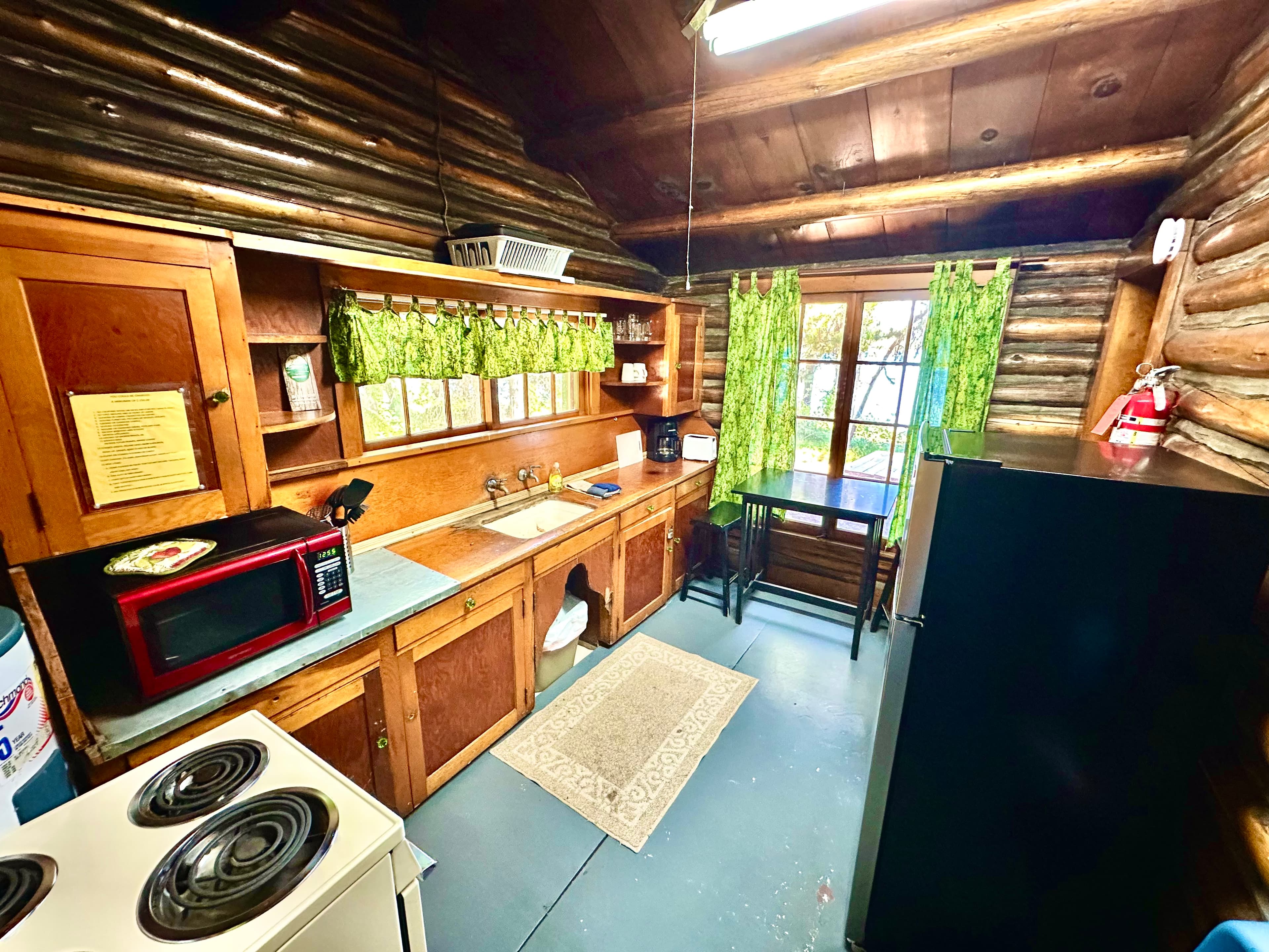 Cozy log cabin kitchen featuring wooden cabinetry, a dining table, and green curtains.