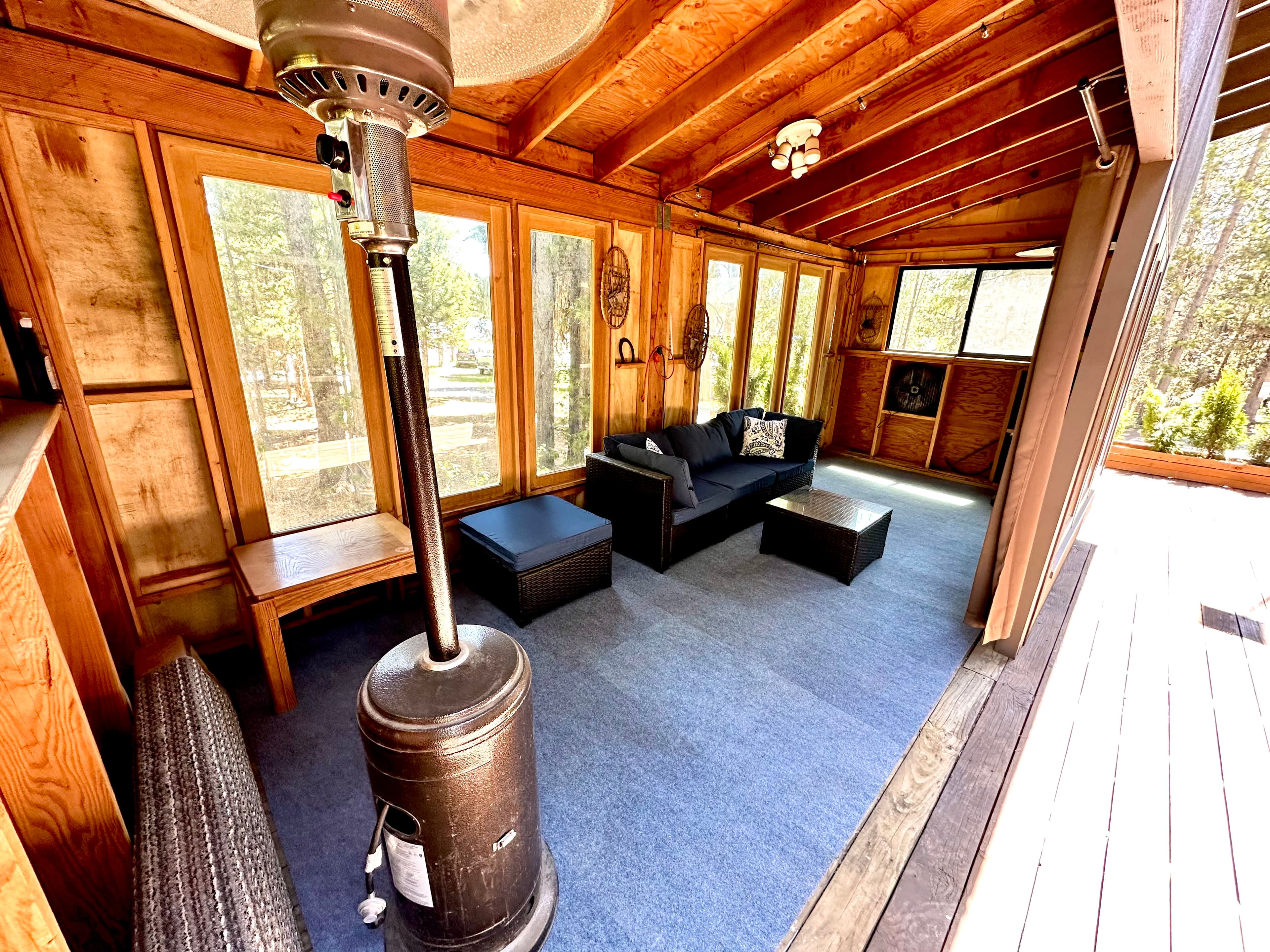 A cozy sunroom featuring large windows, a black sofa, and a central heater.