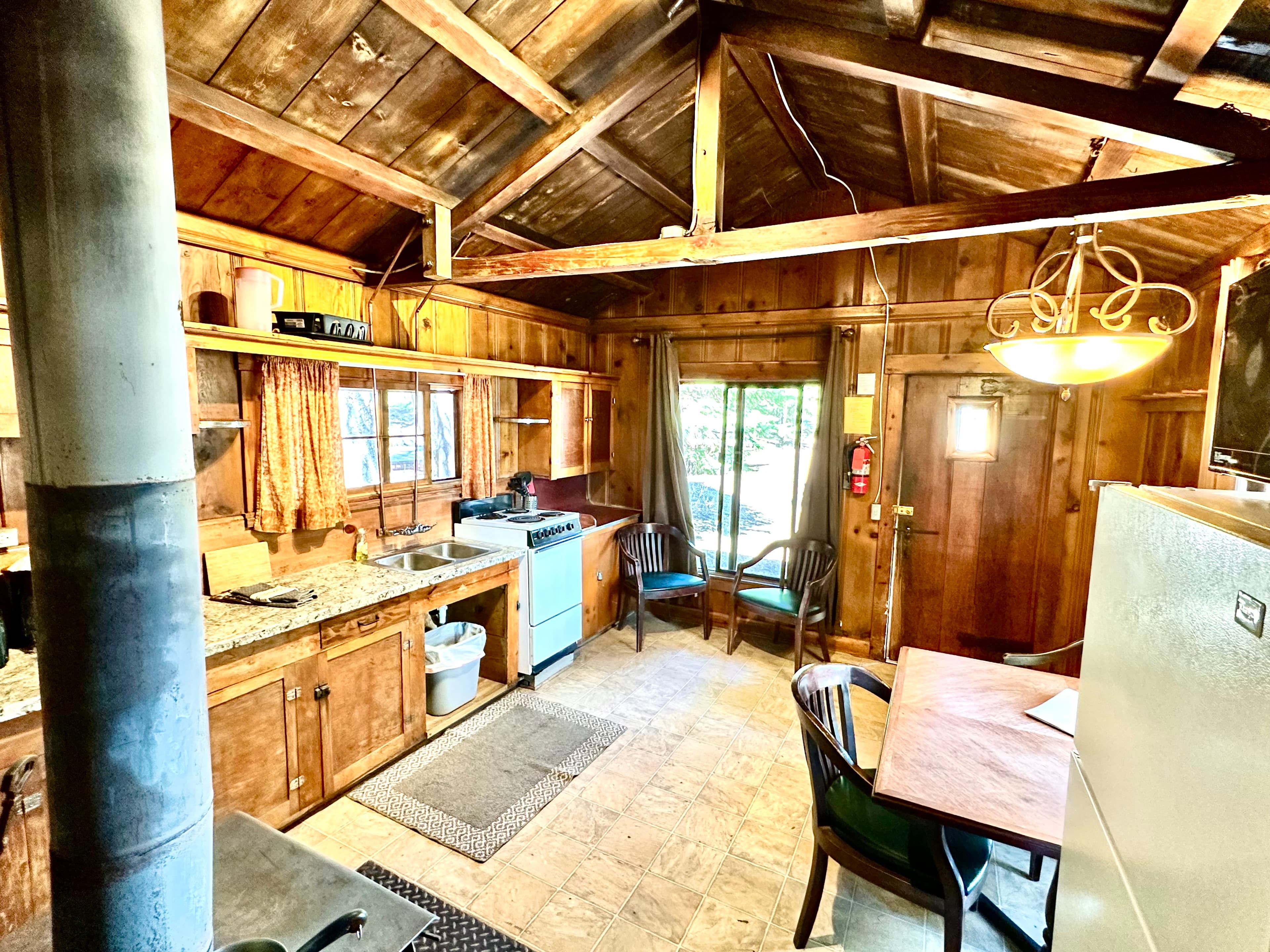 A cozy rustic kitchen with wooden walls, a gas stove, and a small dining area.