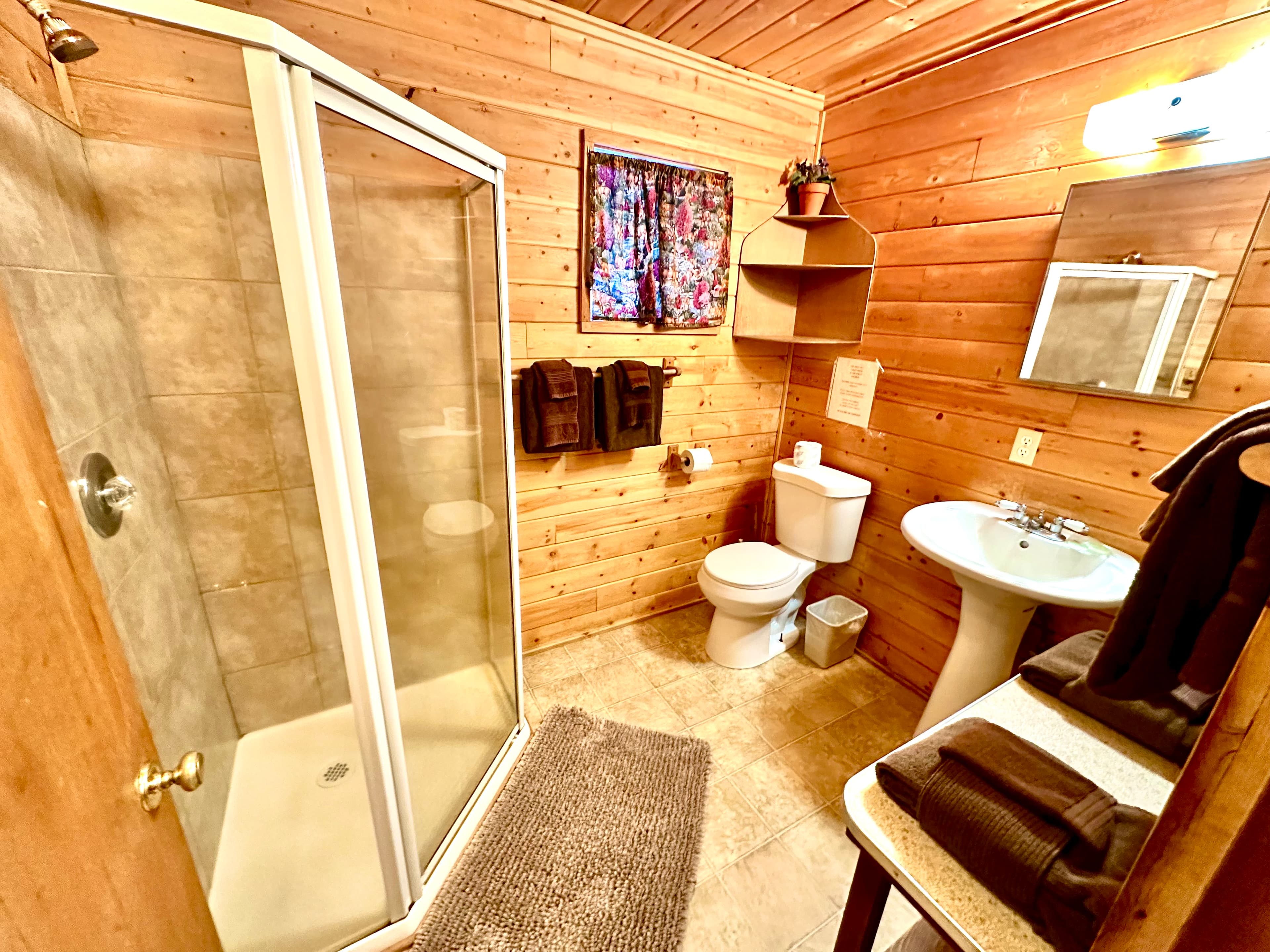 A rustic bathroom featuring a shower, toilet, sink, and wooden accents.