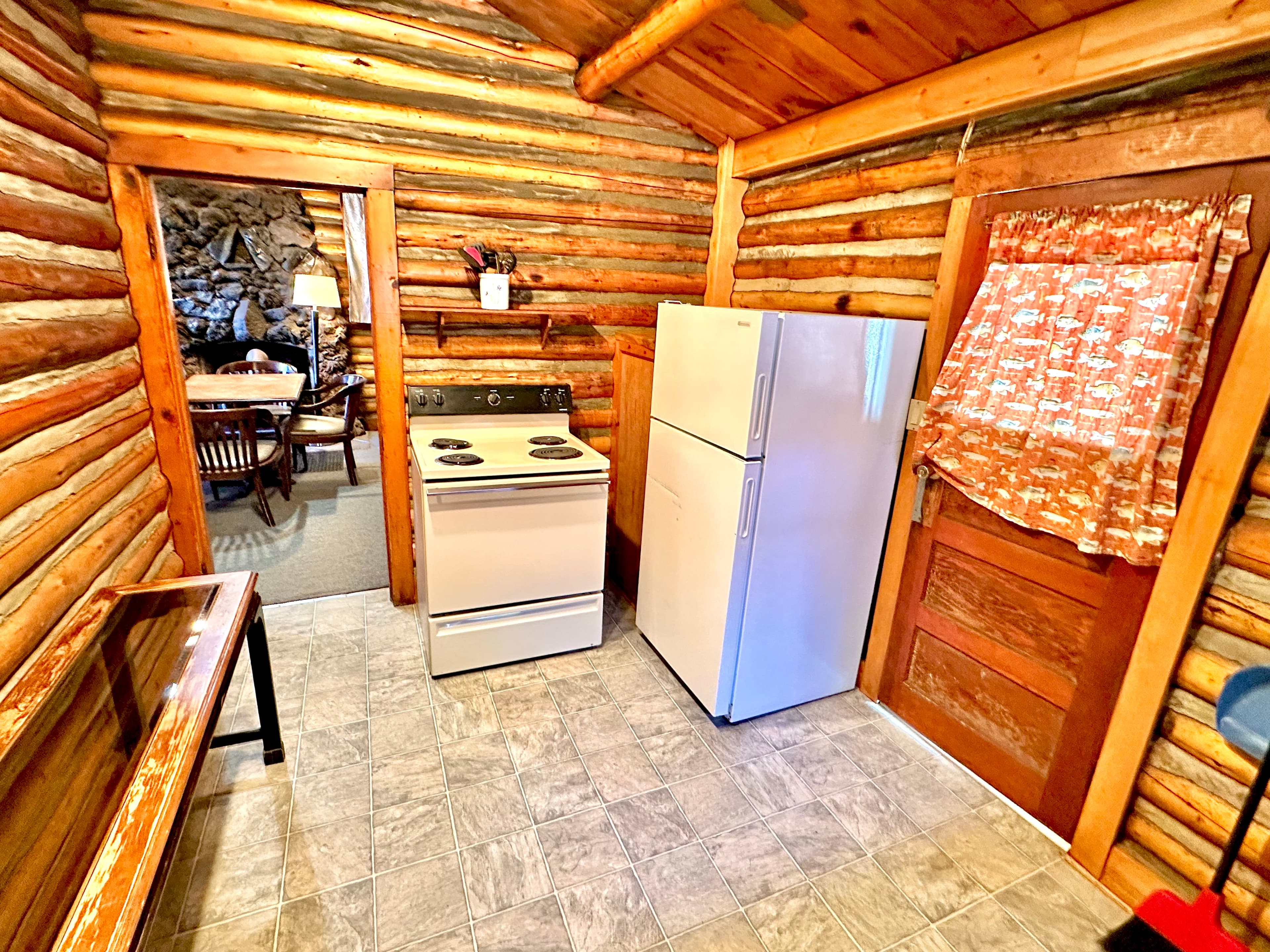 Cozy log cabin kitchen featuring a stove, refrigerator, and wooden finishes.