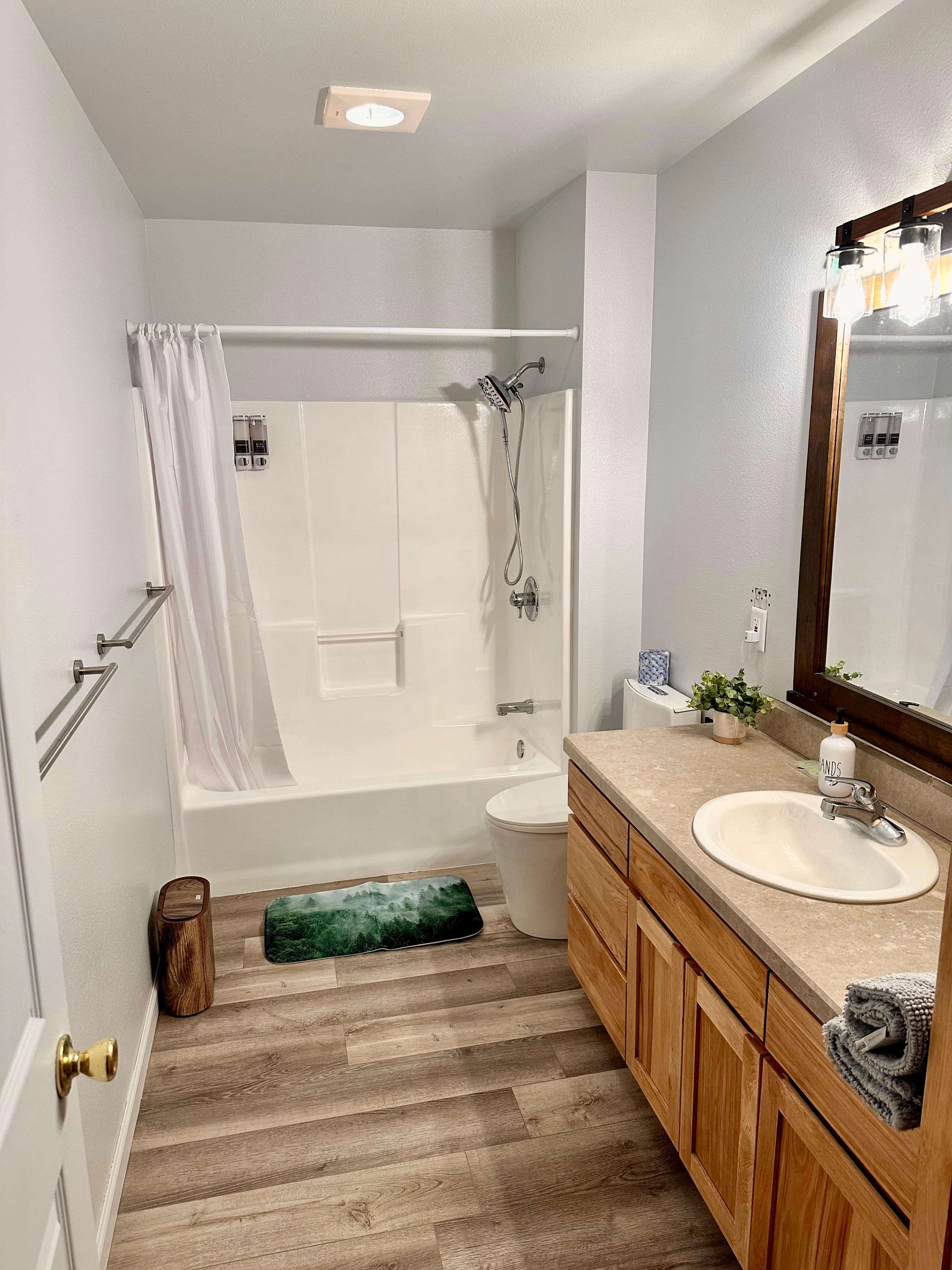 A modern bathroom featuring a bathtub with a shower, a sink with wooden cabinetry, and a decorative rug.
