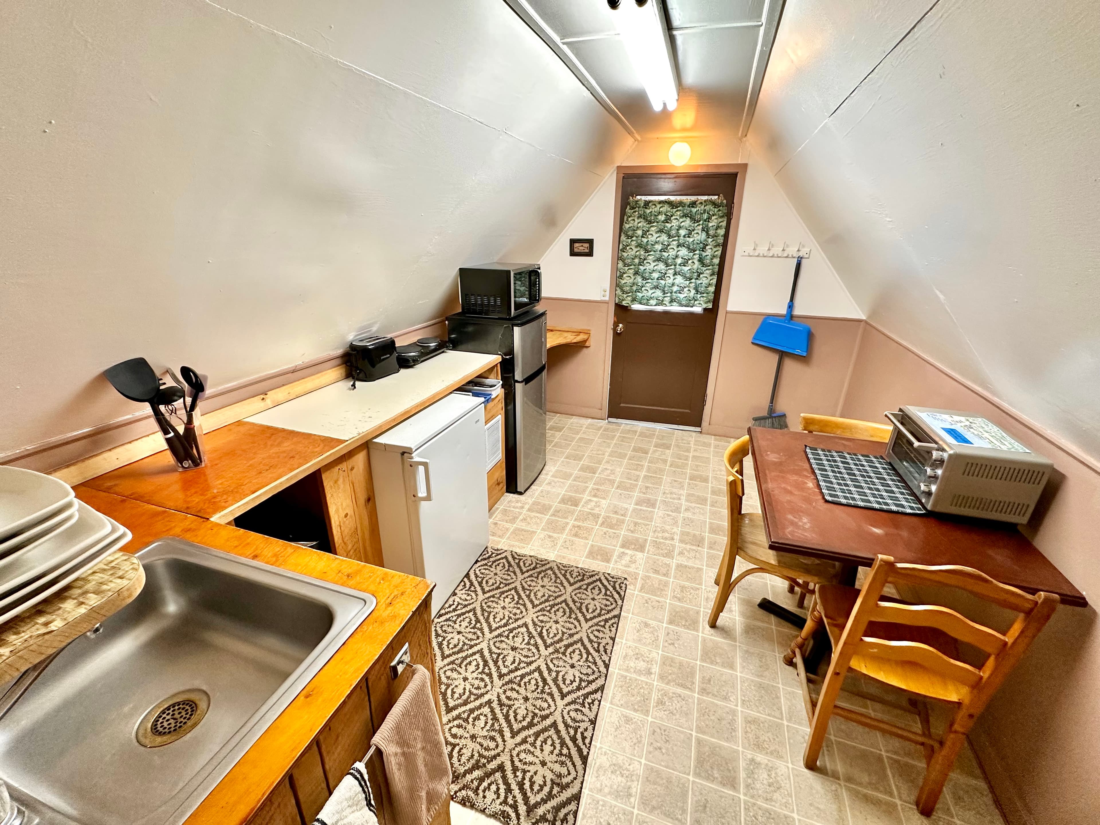 A small attic kitchen with wooden counters, a sink, refrigerator, and a dining table.