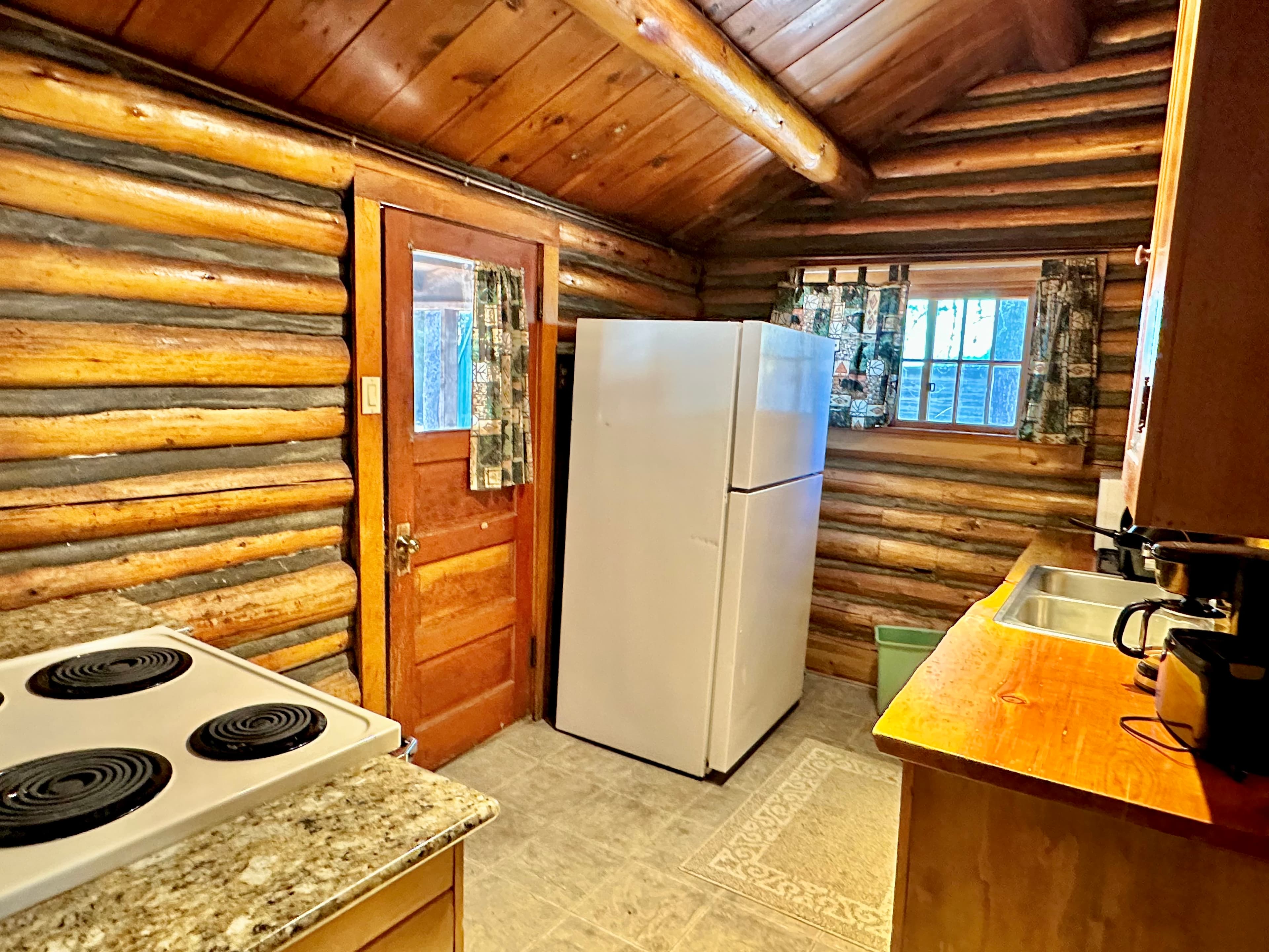 A rustic kitchen with log walls, a white refrigerator, a stove, and wooden counters.