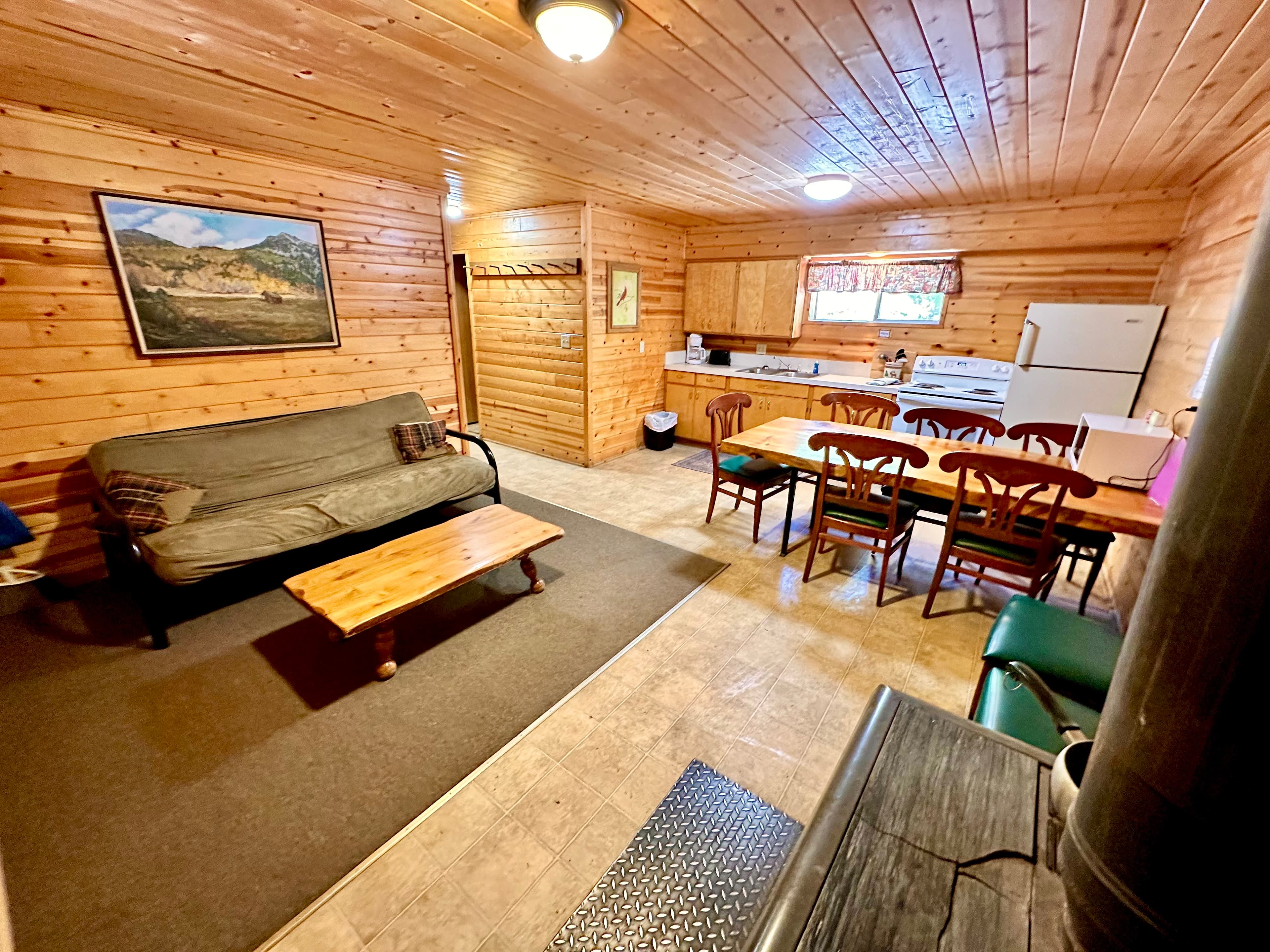 Cozy wooden interior of a cabin featuring a seating area, dining table, and kitchen.