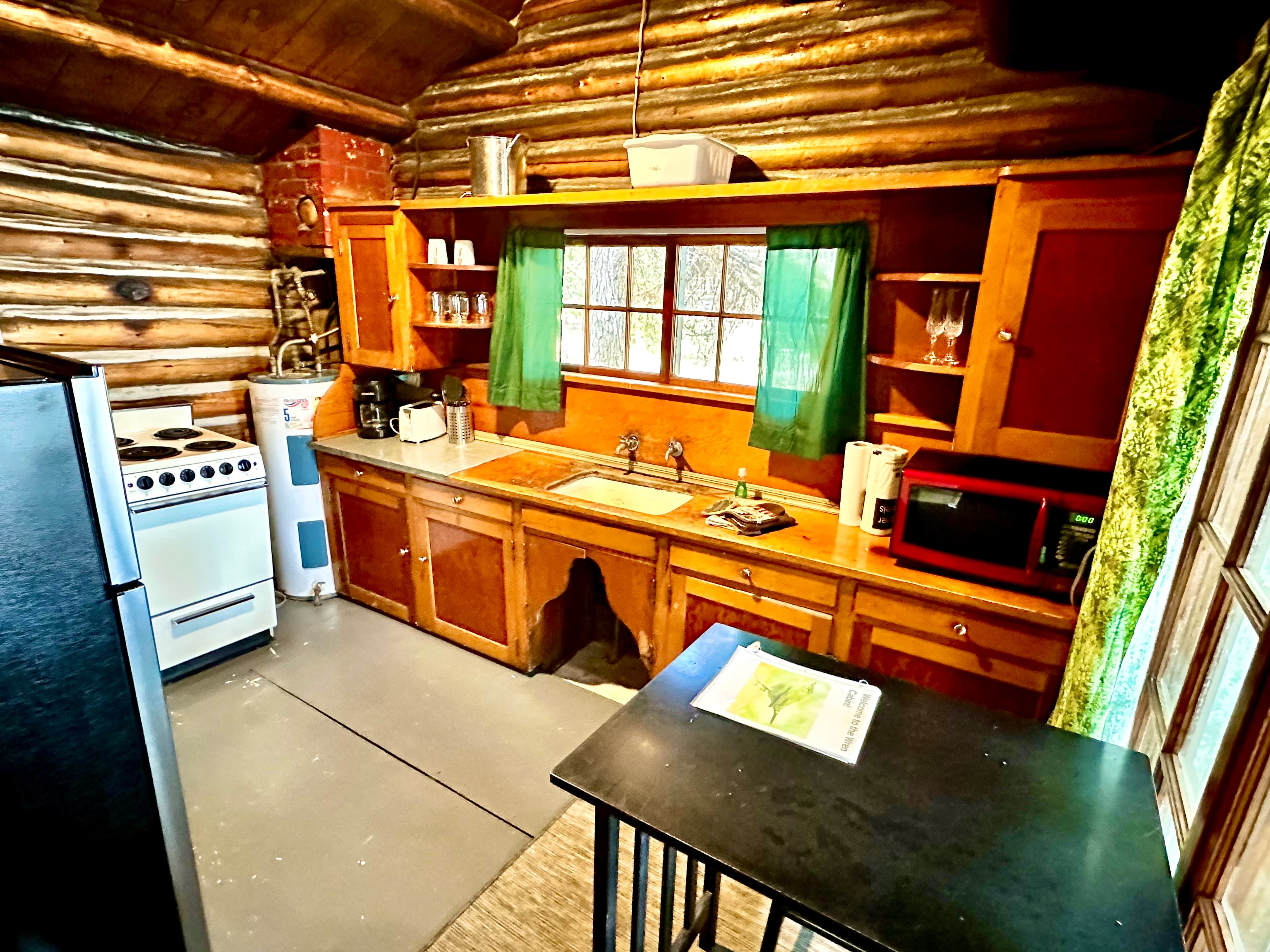 A cozy log cabin kitchen with wooden cabinetry, a stove, microwave, and a small dining table.