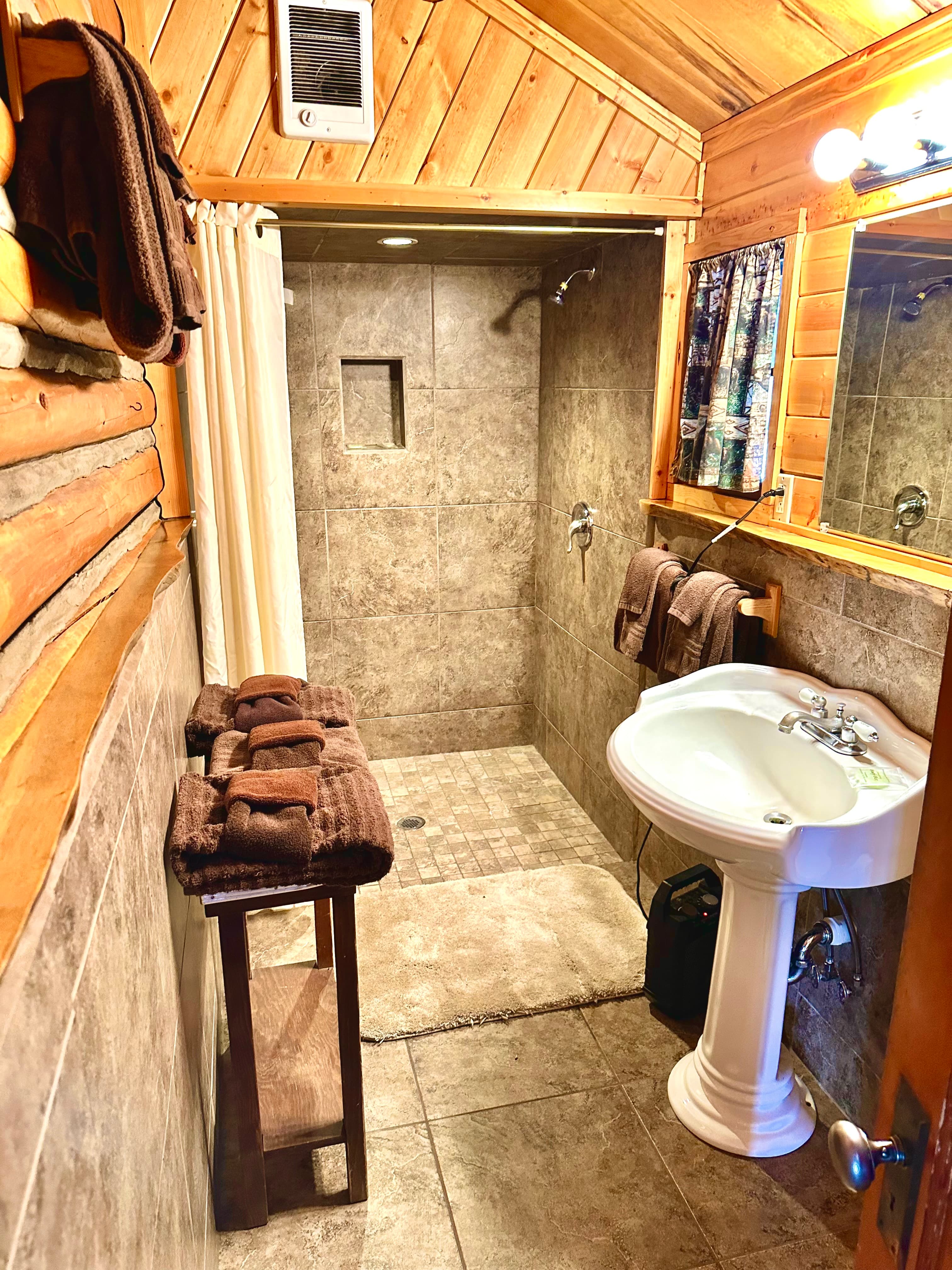 Cozy bathroom featuring a shower, sink, wooden accents, and neatly arranged towels.