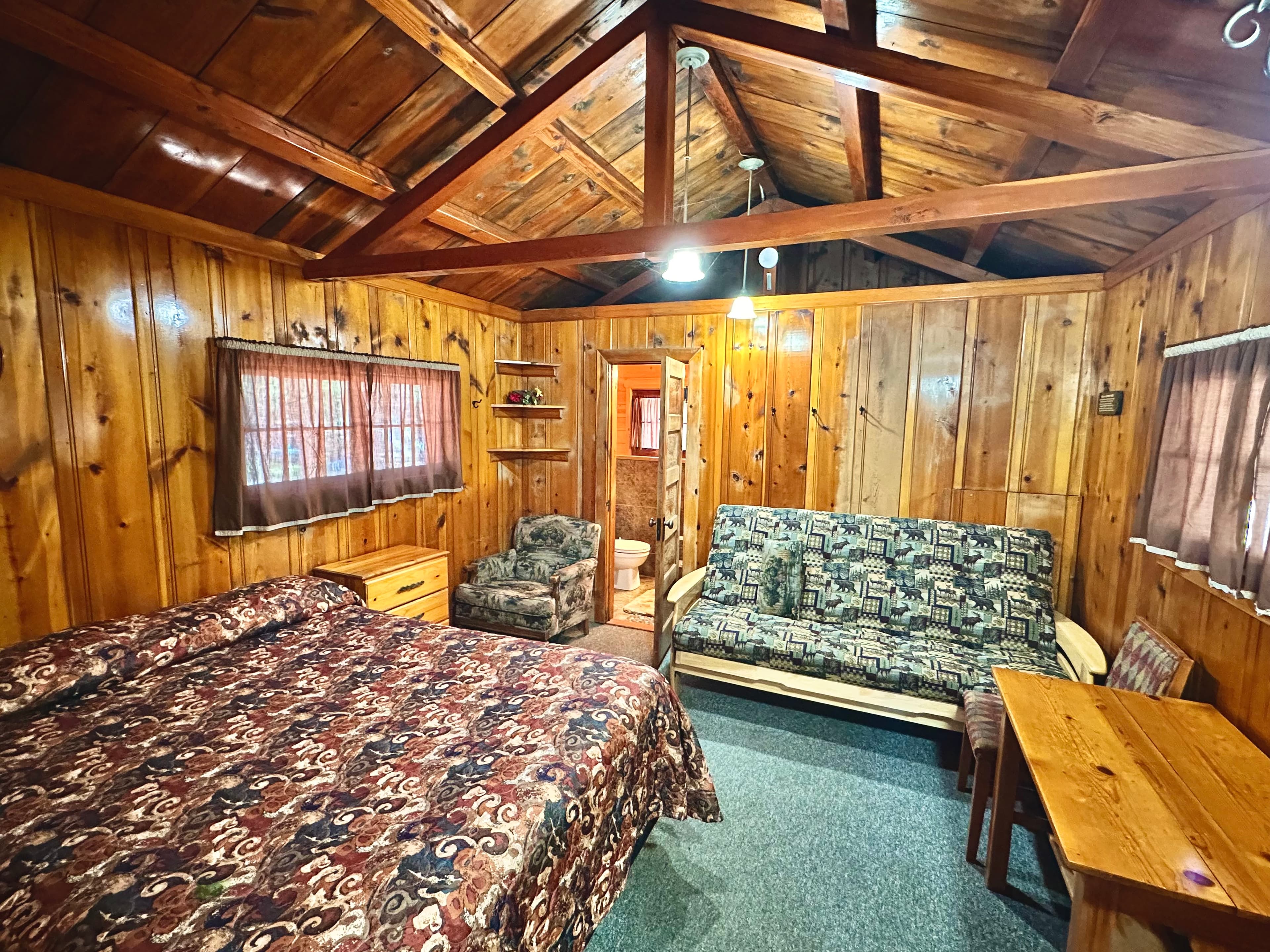 A cozy cabin interior featuring a bed, a sofa, and wooden paneling.