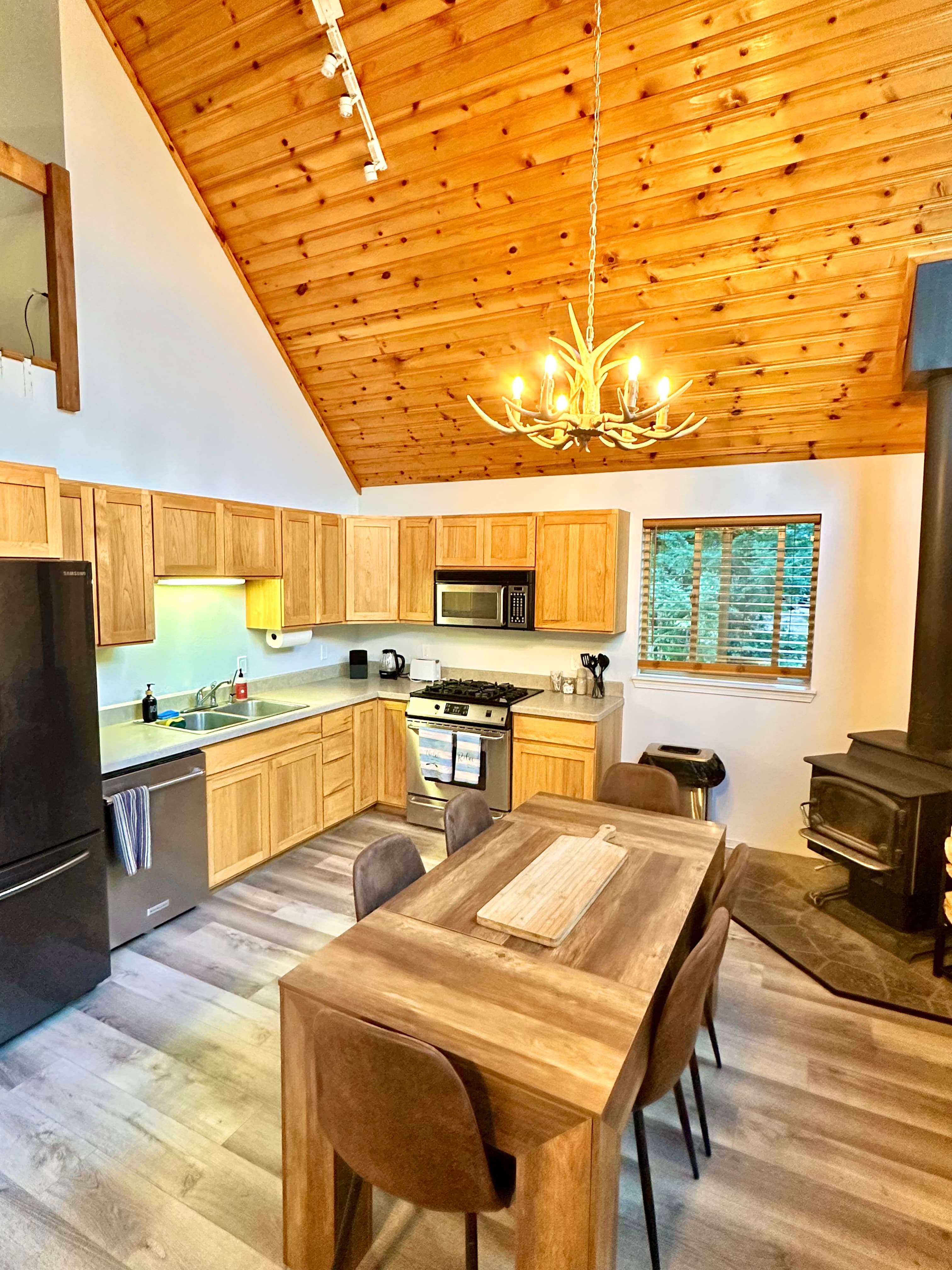 A cozy kitchen with wooden cabinets, a dining table, and a stone fireplace under a vaulted ceiling.