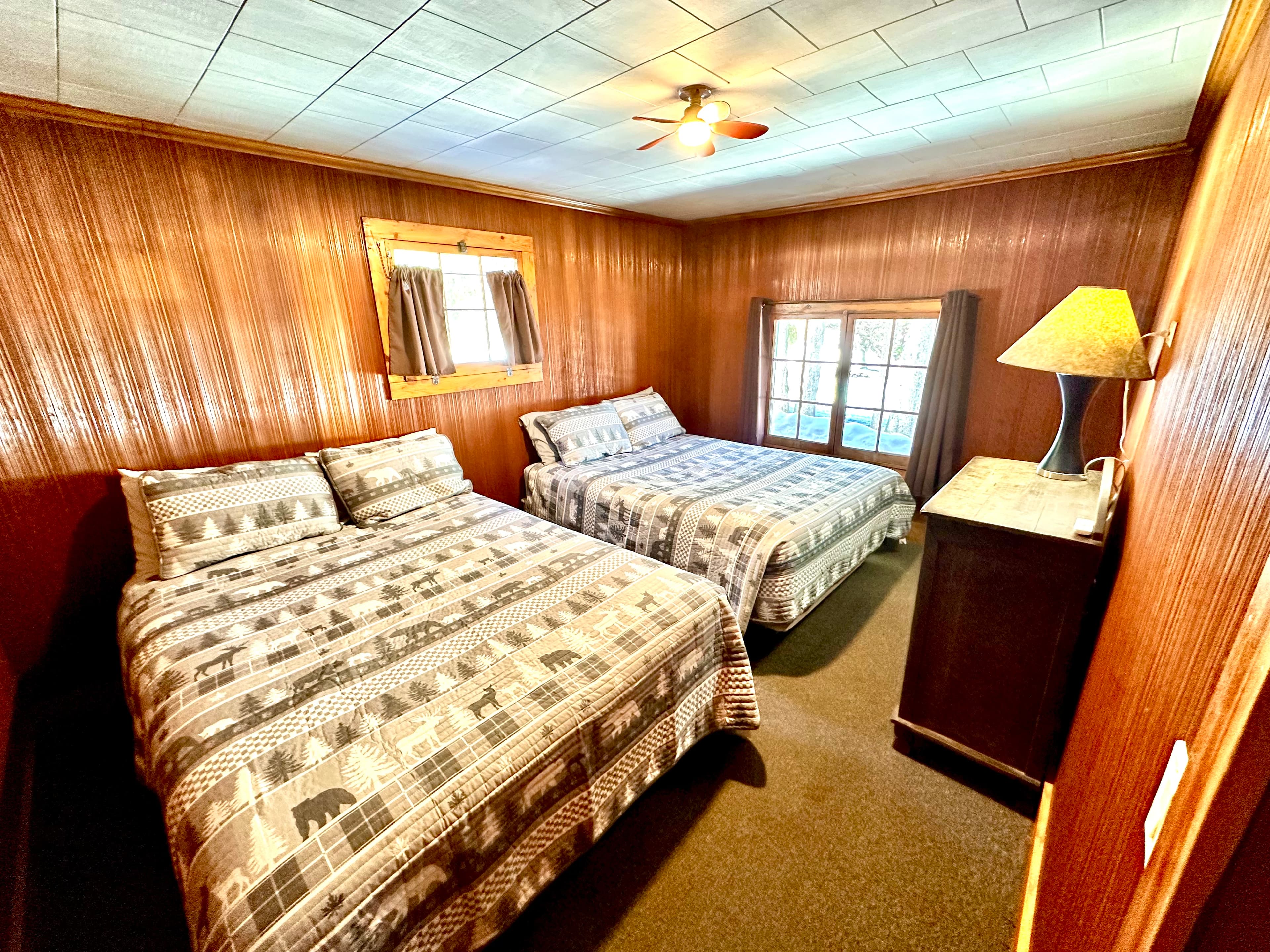 Cozy bedroom featuring two beds with patterned bedding, a lamp, and a window.