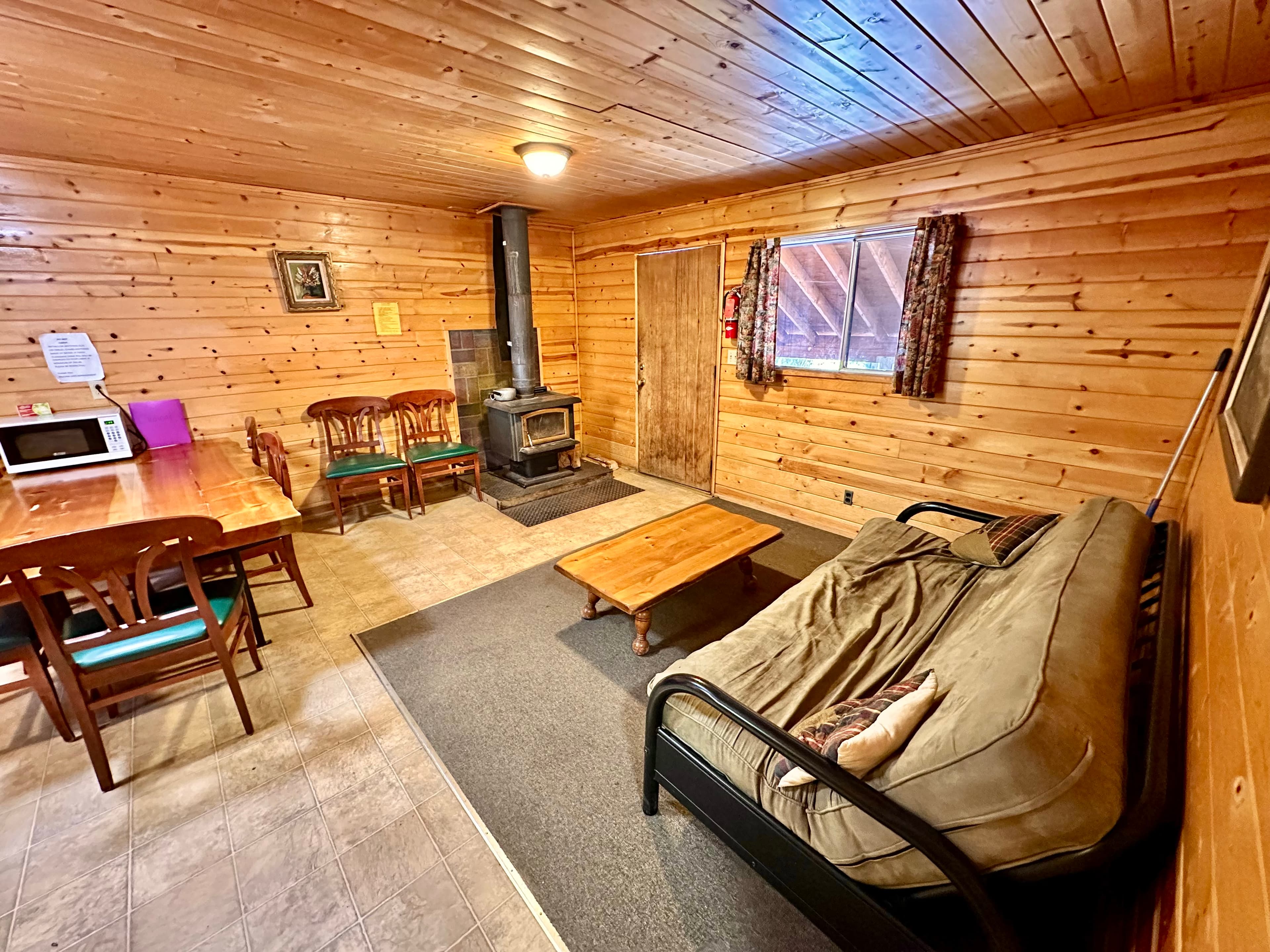 Cozy wooden cabin interior featuring a seating area, dining table, and a wood stove.