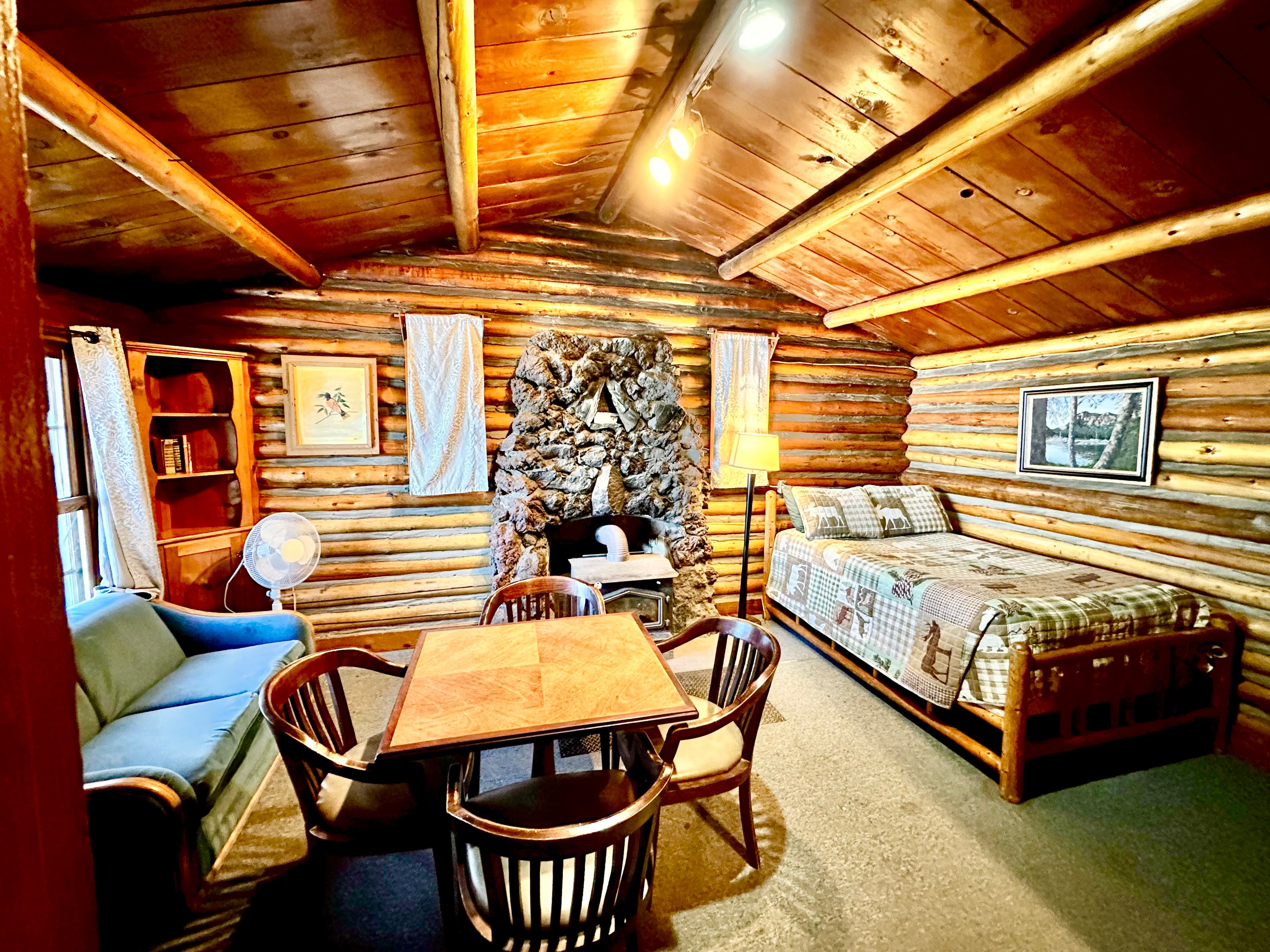 Cozy log cabin interior featuring a bed, seating area, and a stone fireplace.