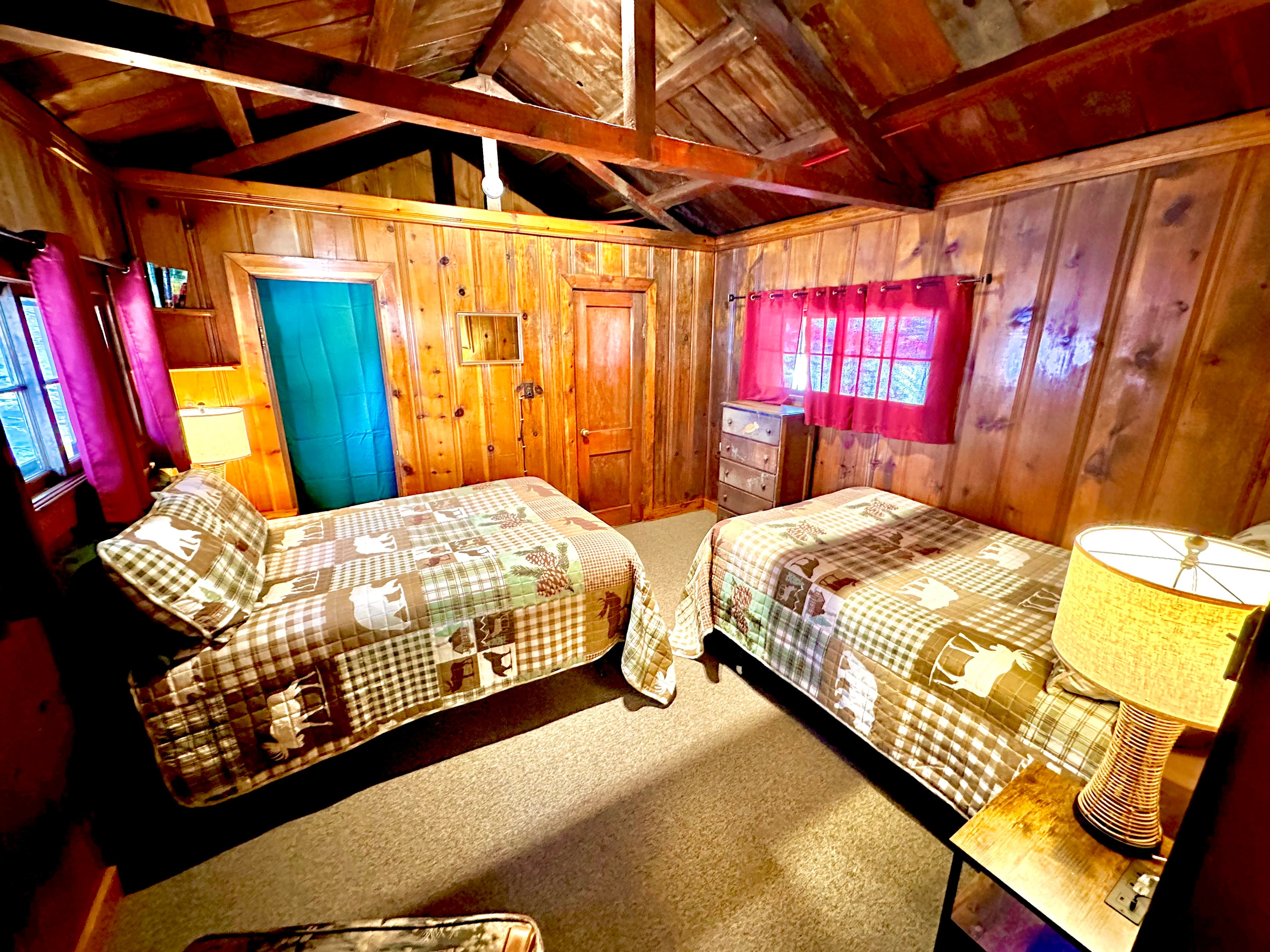 A cozy rustic bedroom with two quilts on beds, wooden walls, and warm lighting.