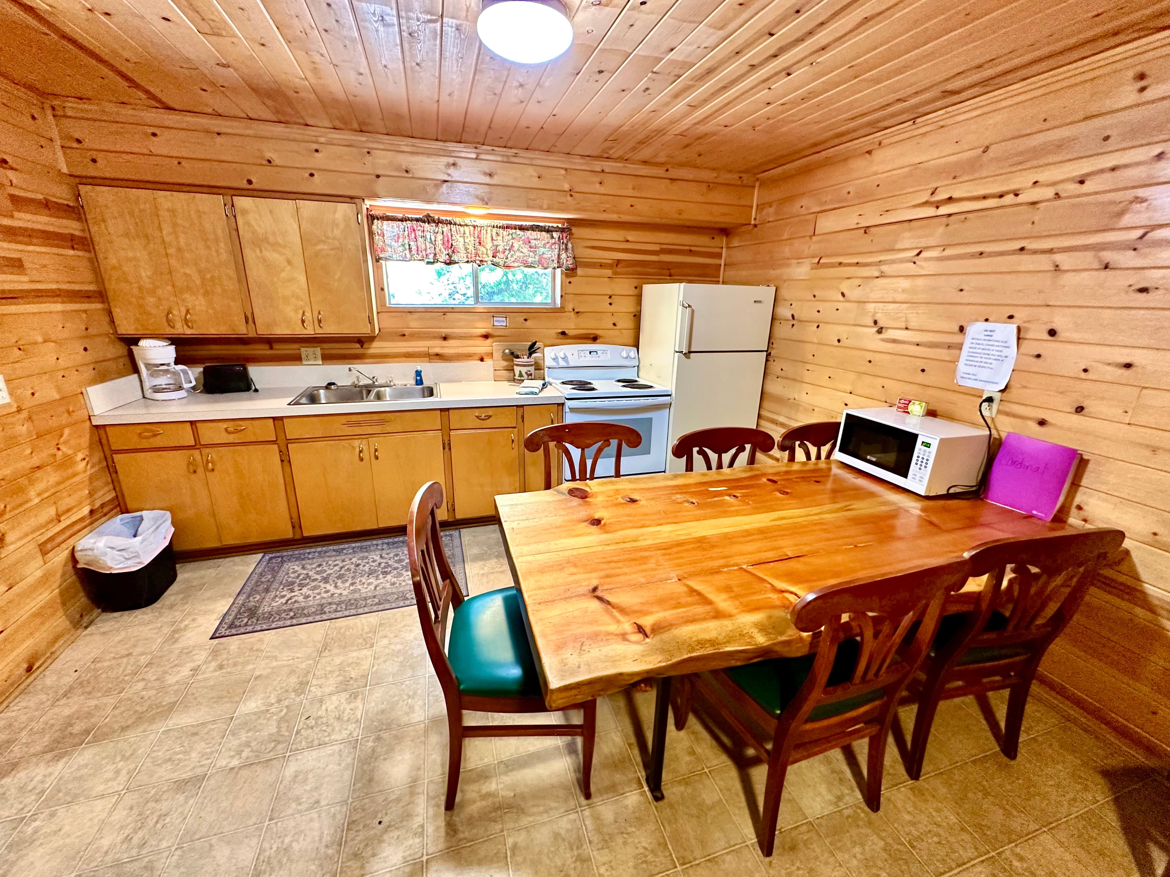 A cozy wooden kitchen featuring a dining table with six chairs, cabinets, and essential appliances.