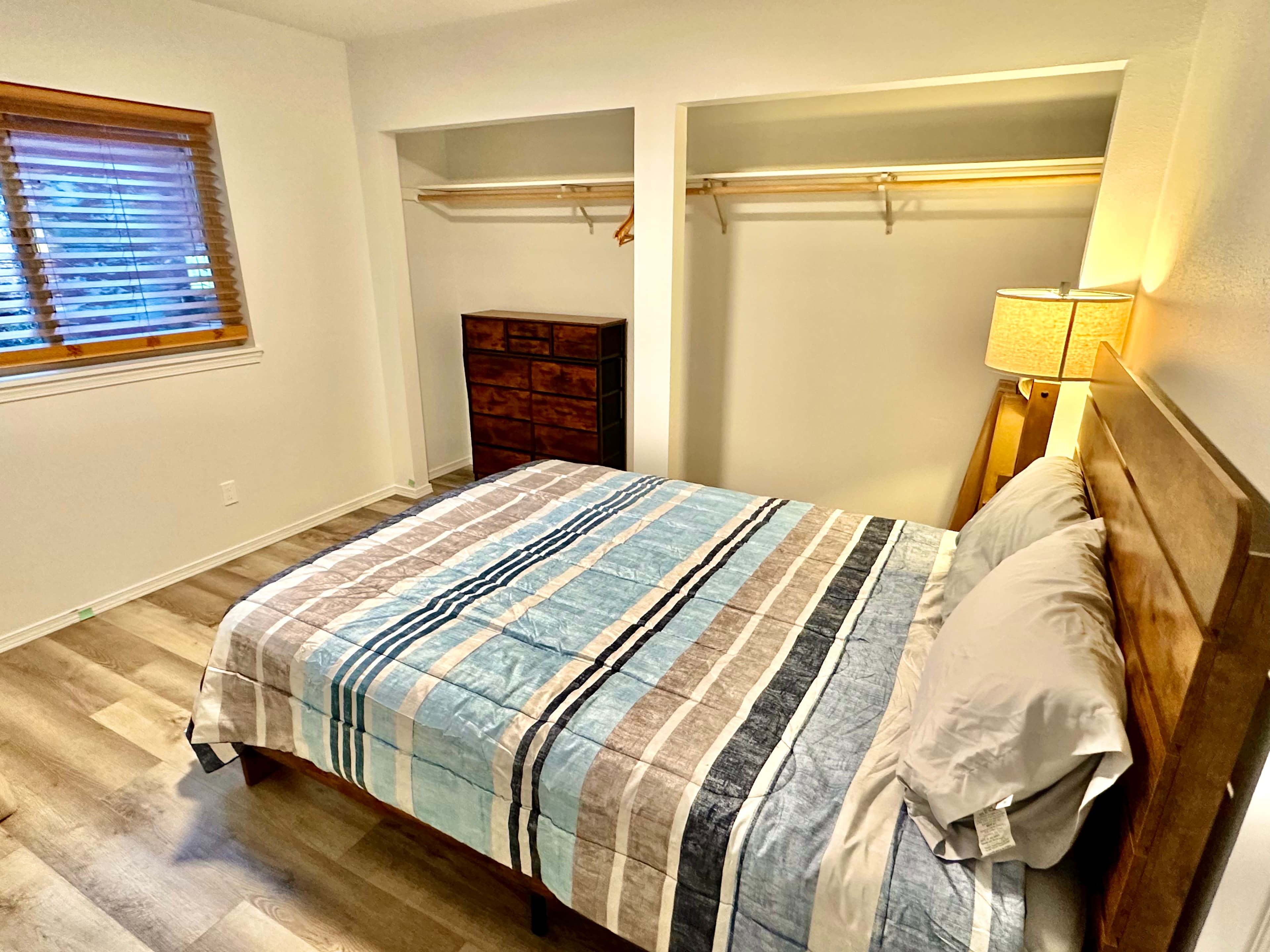 A cozy bedroom featuring a striped bedspread, wooden furniture, and ample natural light.