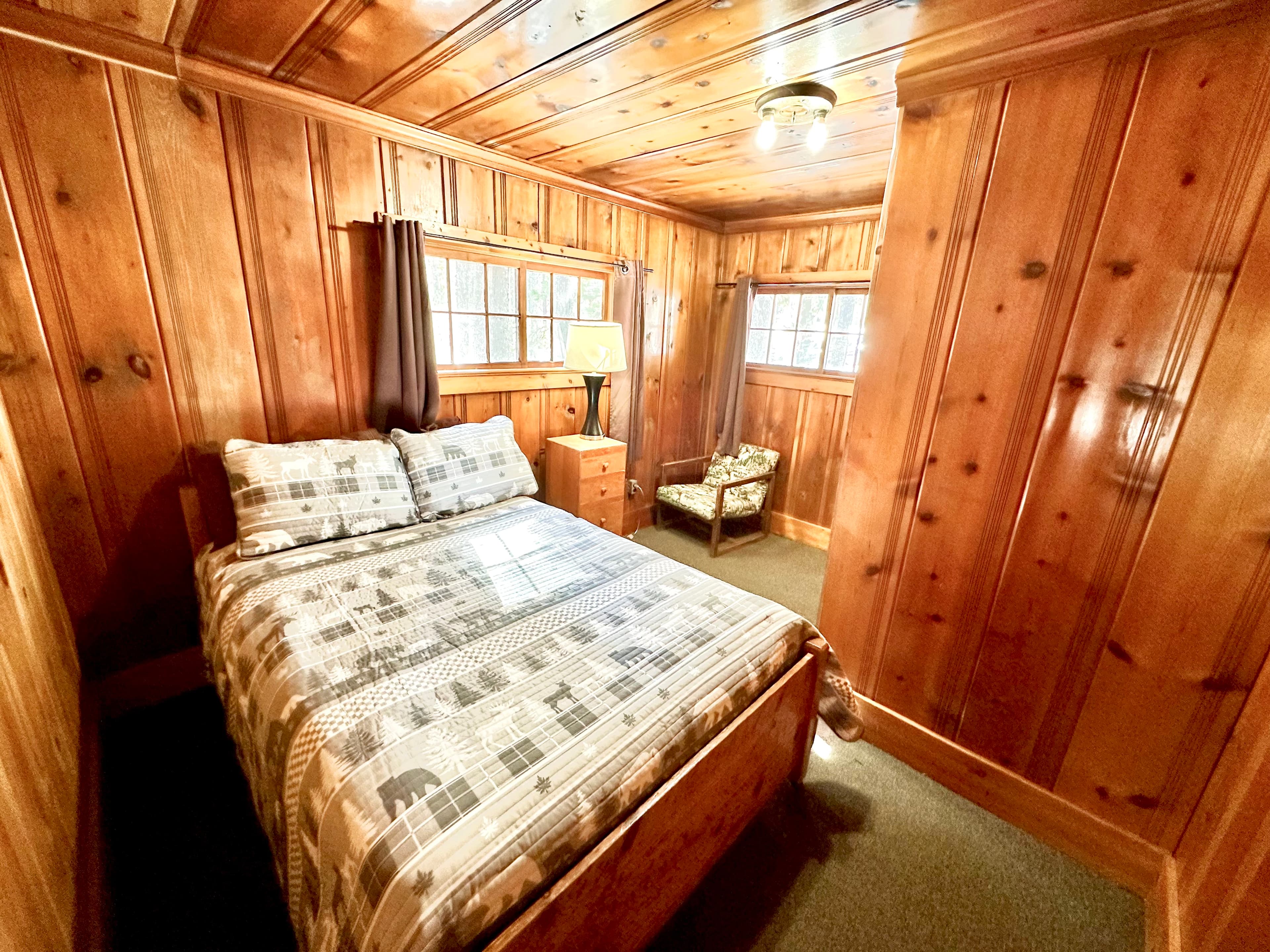 Cozy wooden-paneled bedroom featuring a double bed, bedside table, and armchair.