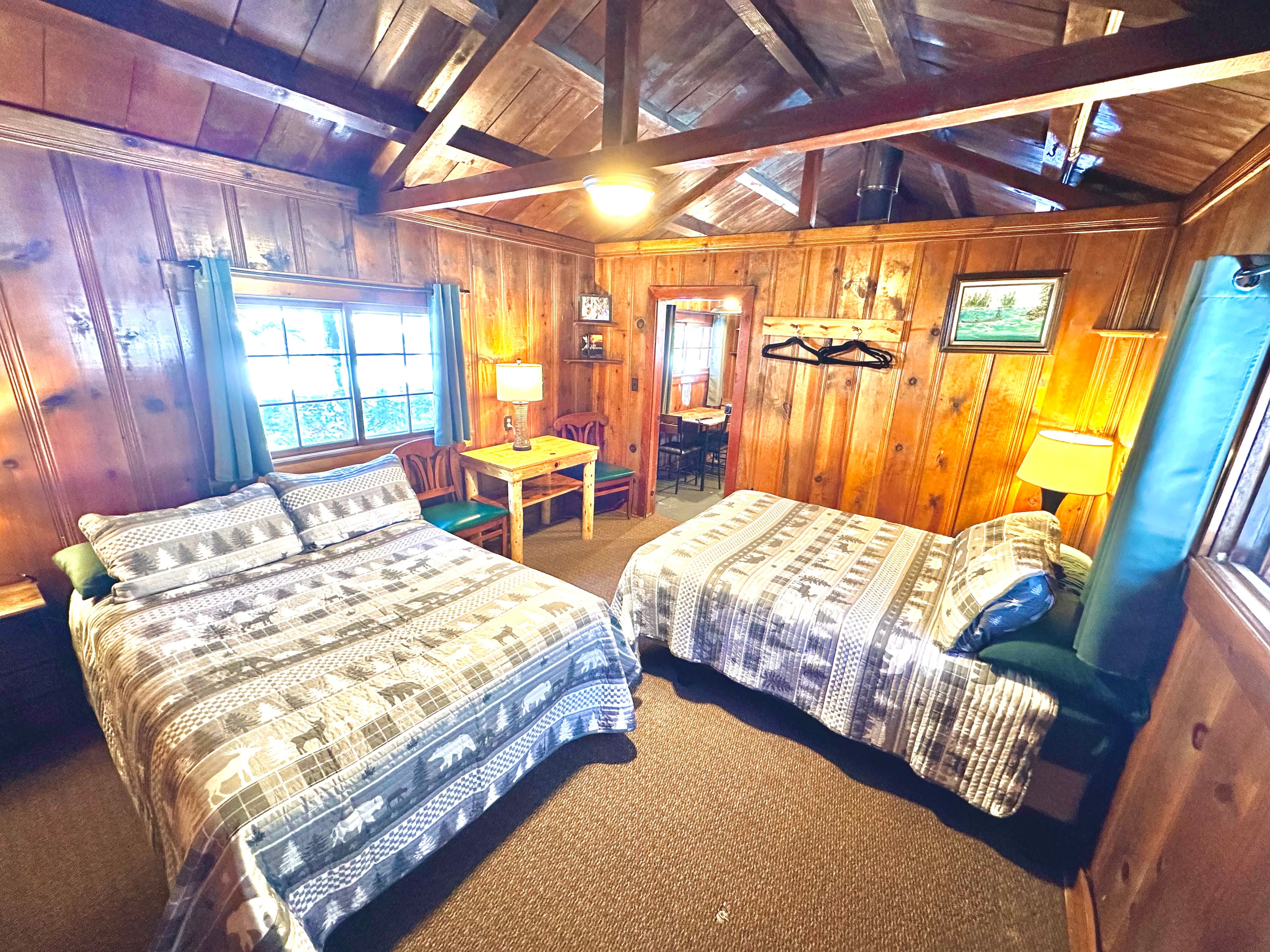A cozy wooden cabin room featuring two beds, a table, and rustic decor.