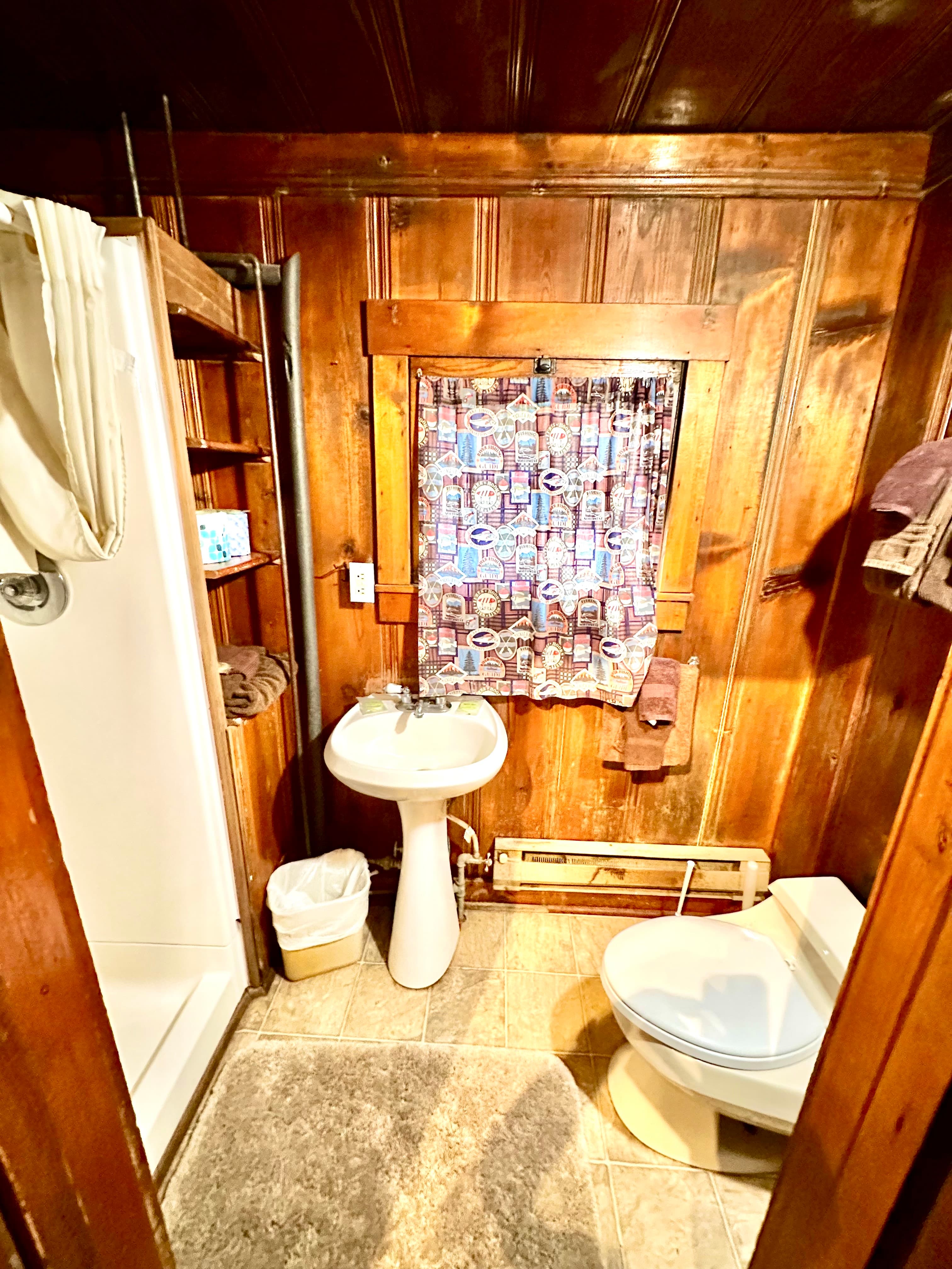 A small bathroom featuring a shower, sink, toilet, and wooden paneling.