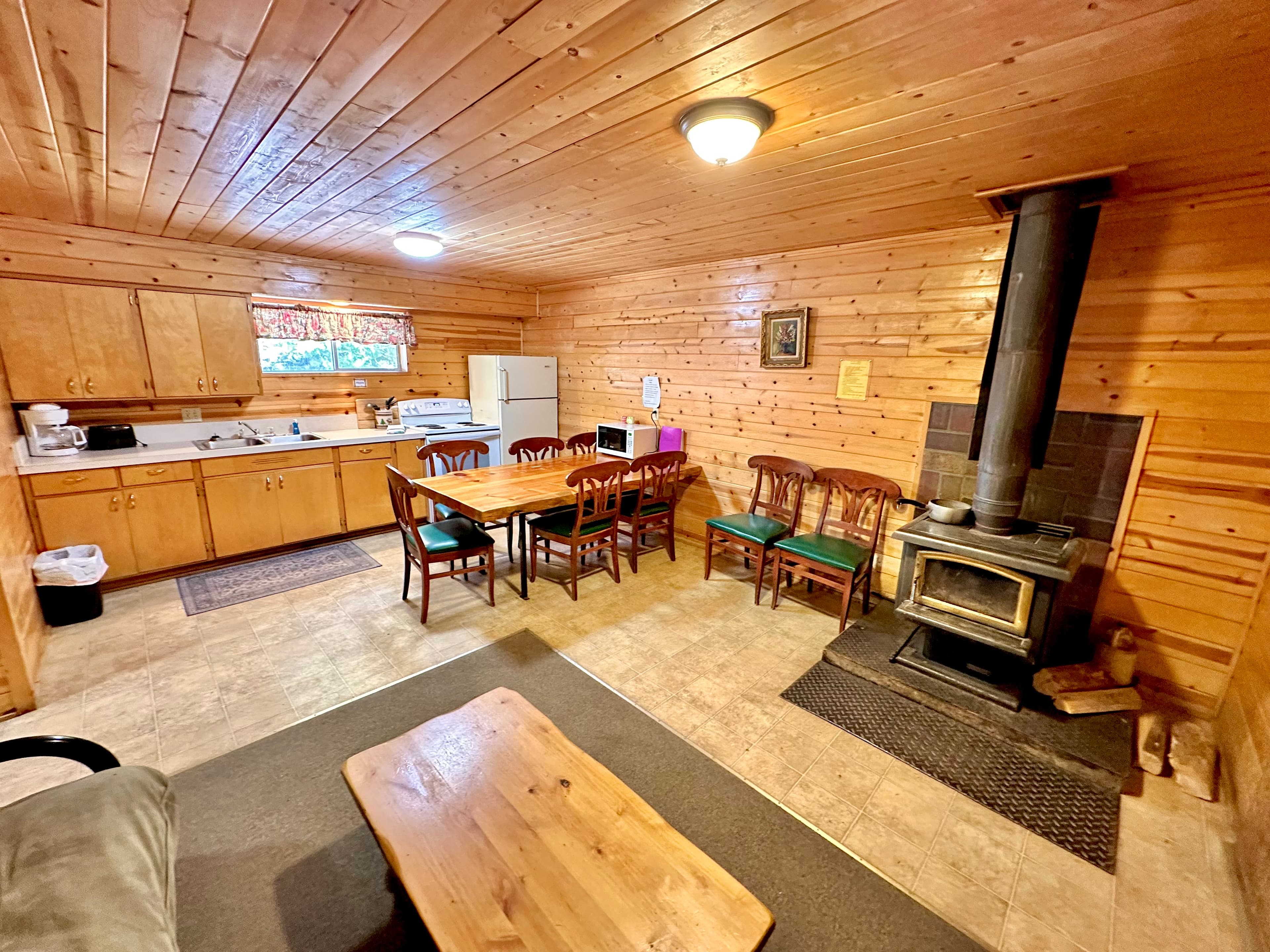 A cozy wooden kitchen and dining area featuring a table, chairs, stove, and refrigerator.