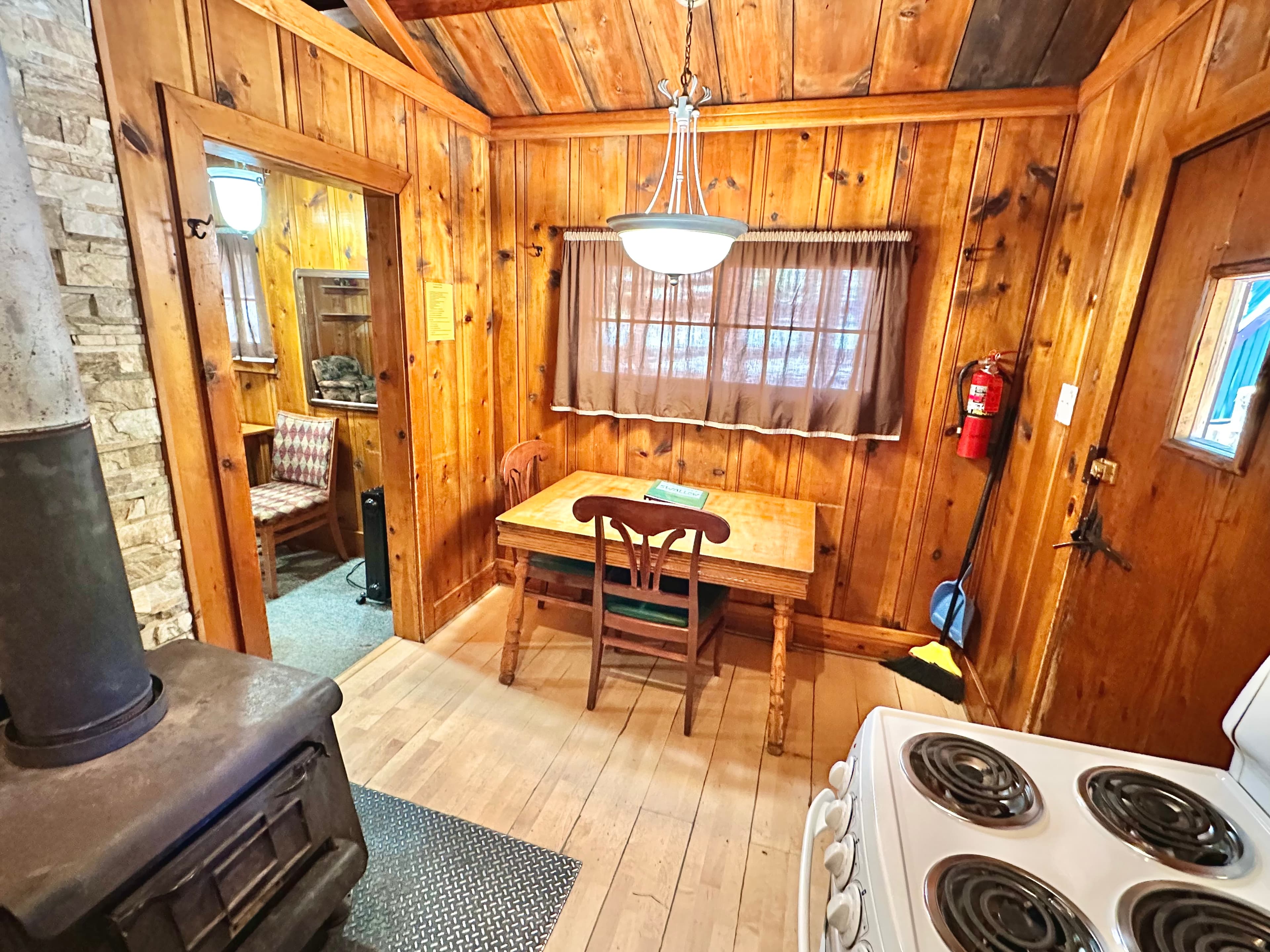 A rustic wooden kitchen with a dining table, stove, and a cozy chair in the background.