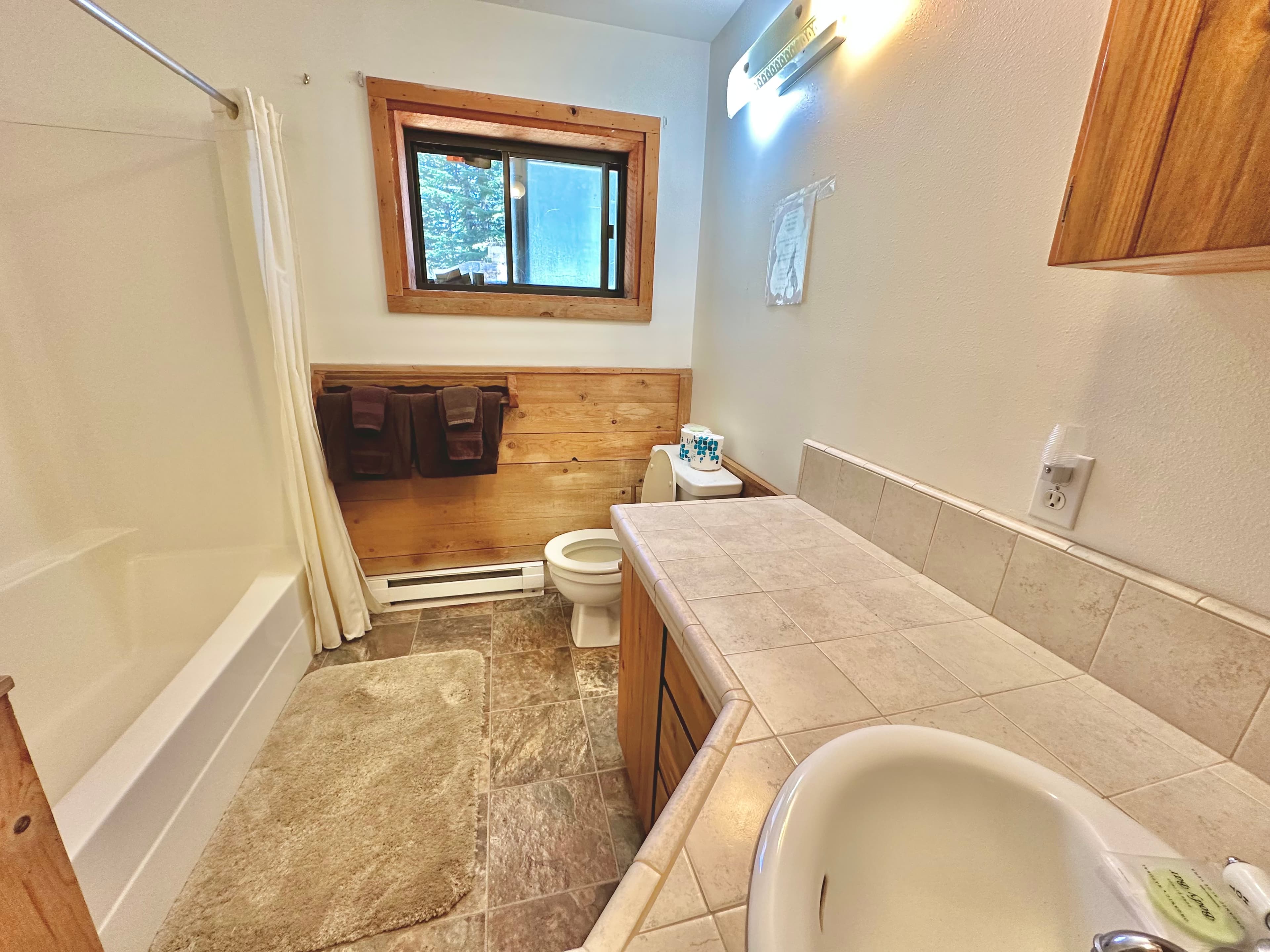 A bright, modern bathroom featuring a tub, toilet, and wooden accents.
