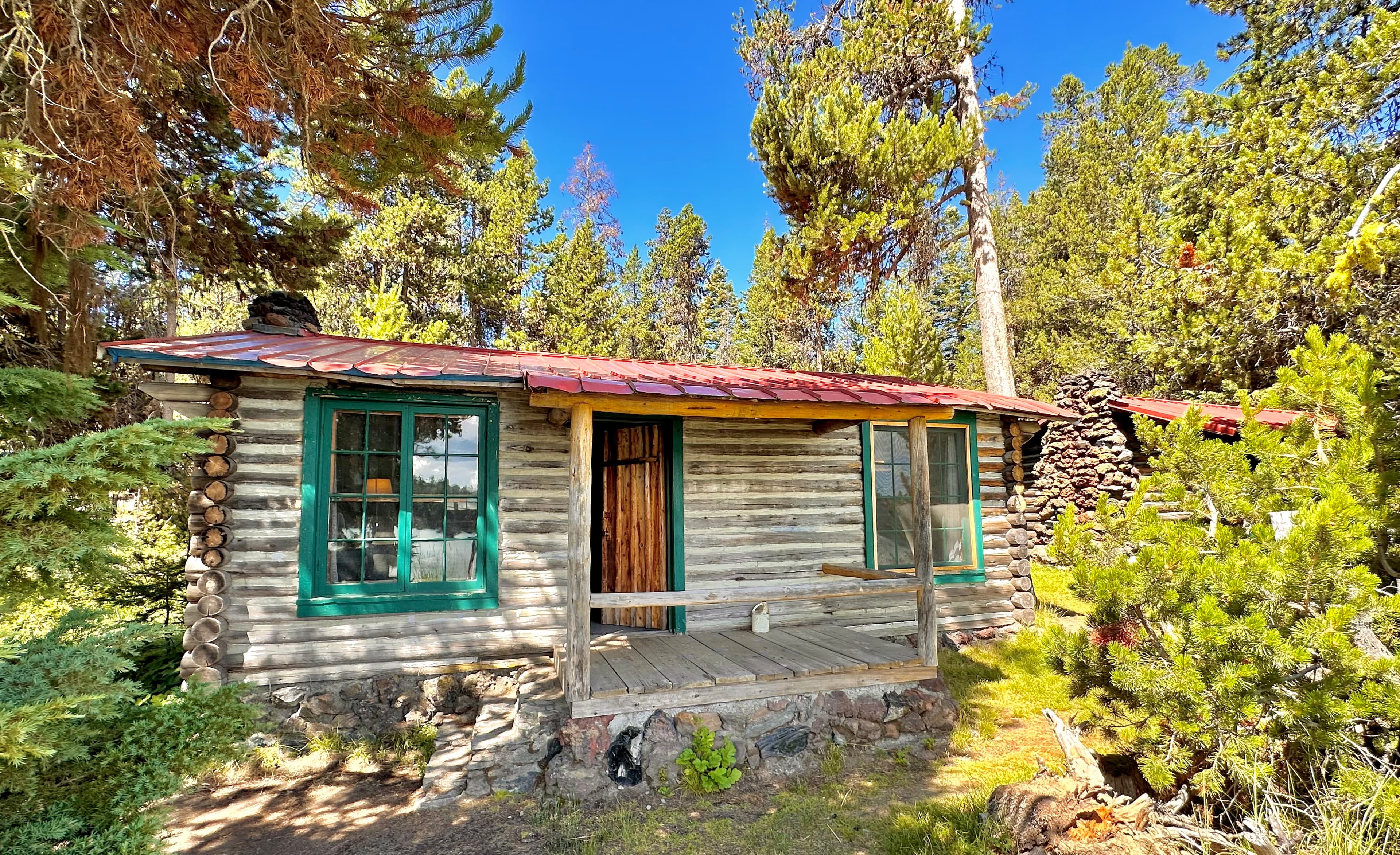 A rustic cabin surrounded by tall trees and greenery.