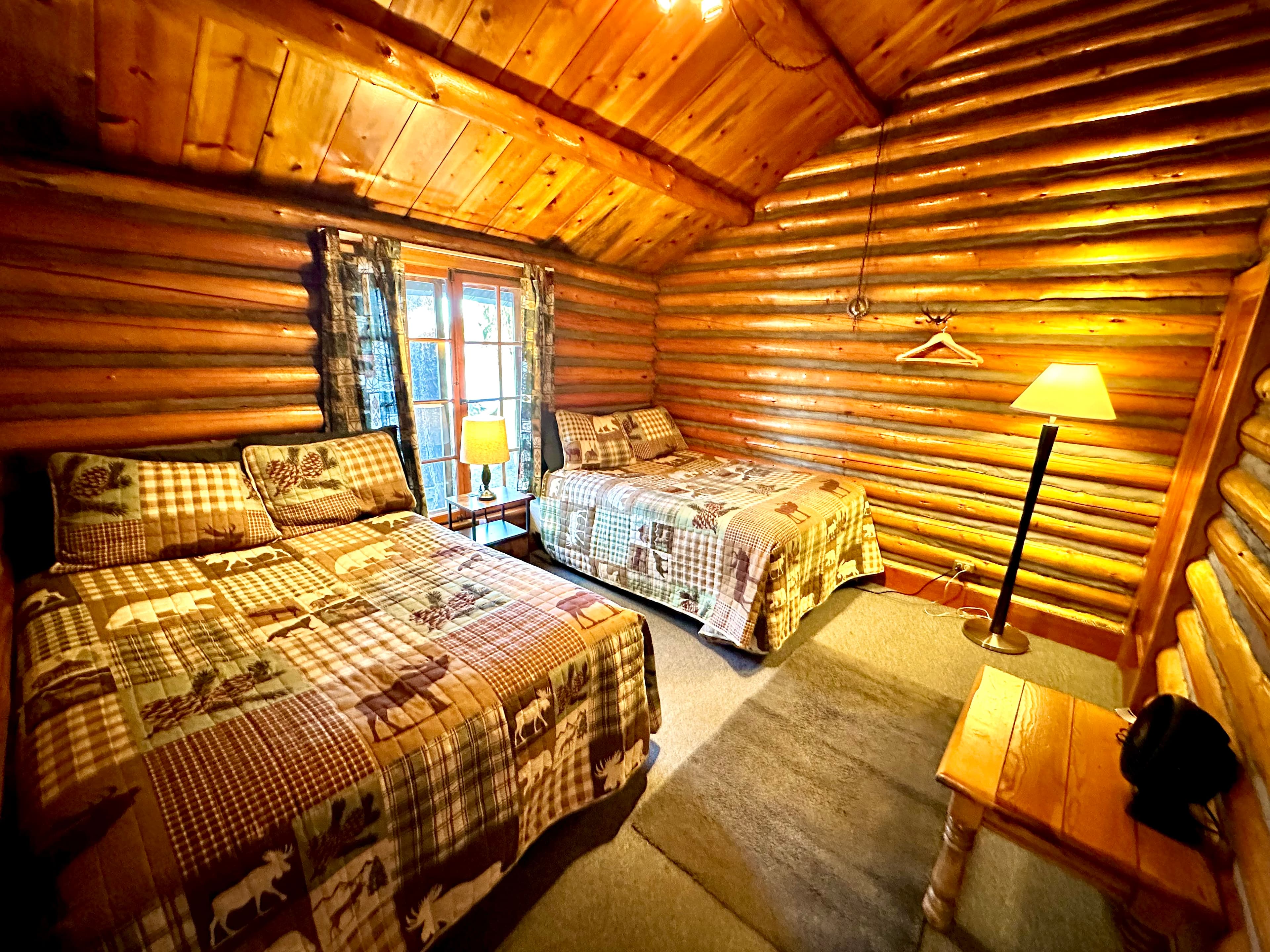 Cozy cabin interior with two beds, wood paneling, and warm lighting.