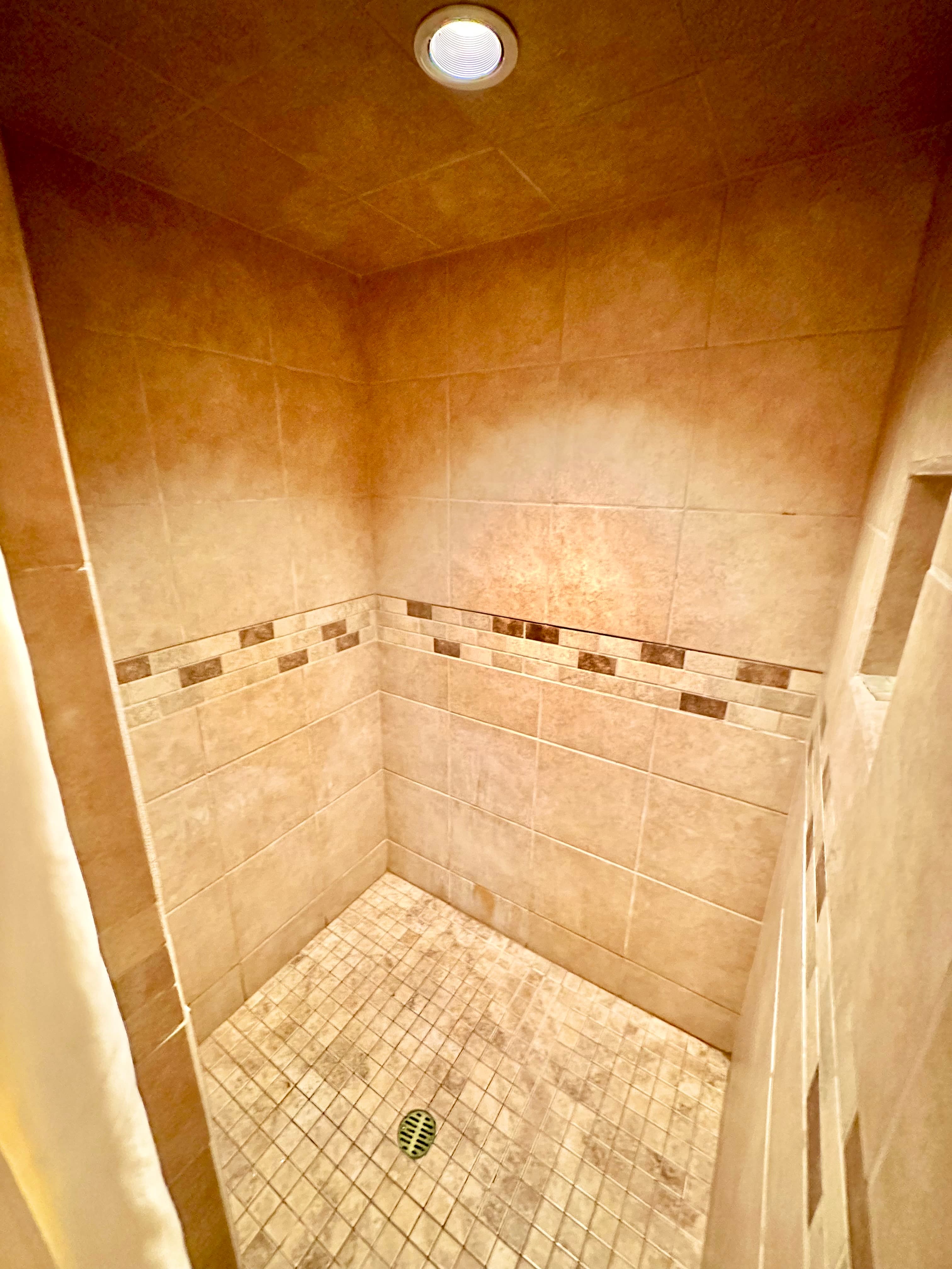 A small, tiled shower stall with a central drain and a light fixture on the ceiling.